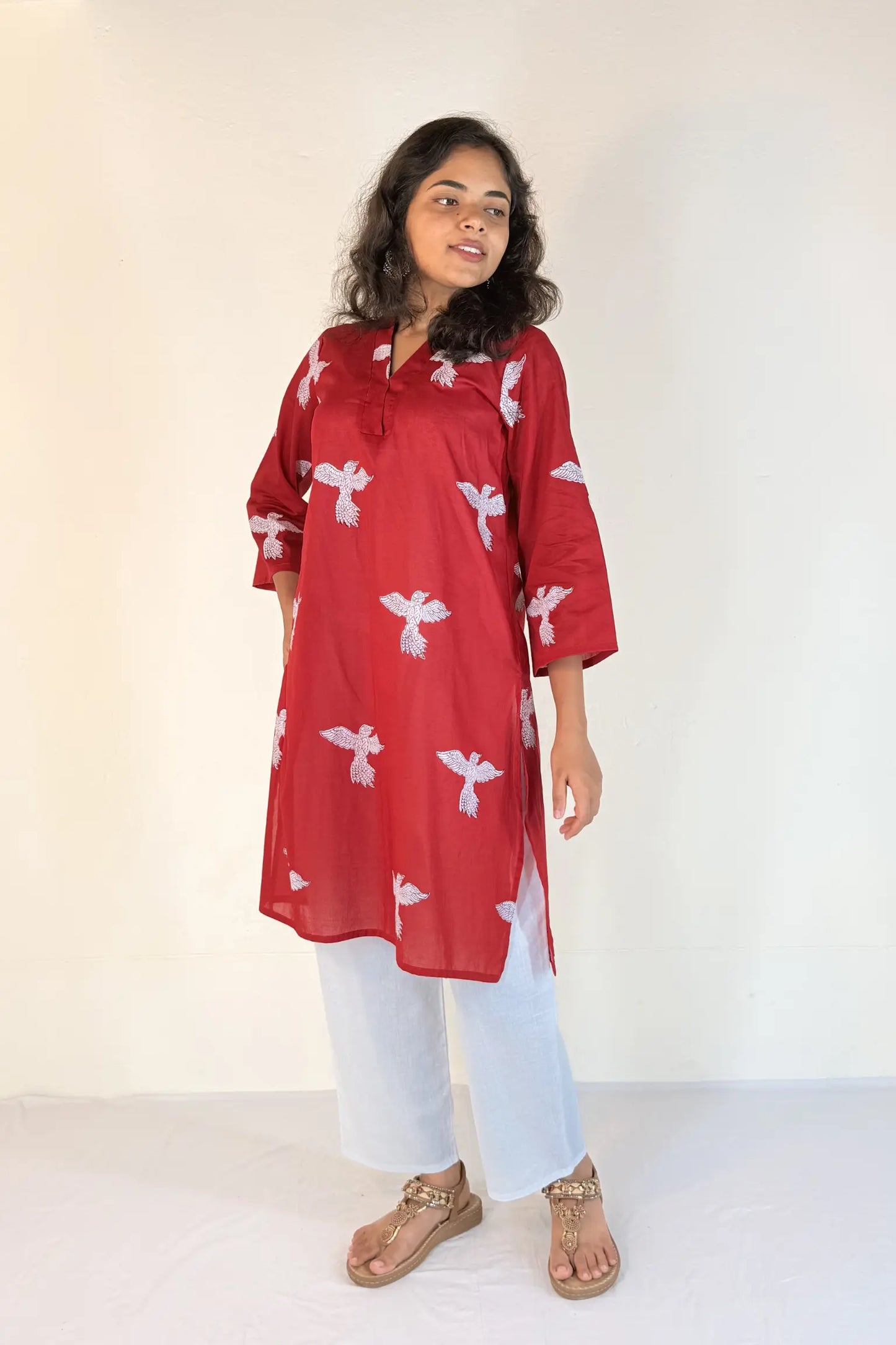 Woman wearing a red kurta with white patterns on a plain background