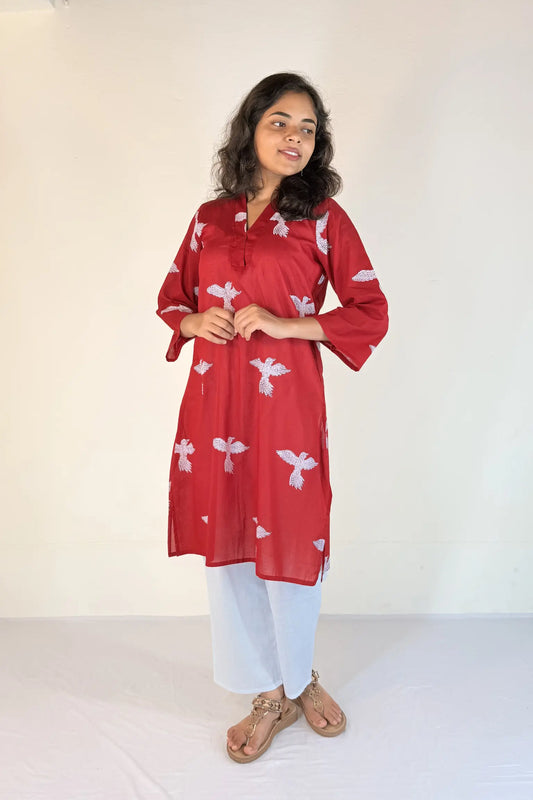Woman wearing a red kurta with white patterns on a plain background