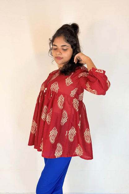 Woman wearing a red patterned top and blue pants against a white background