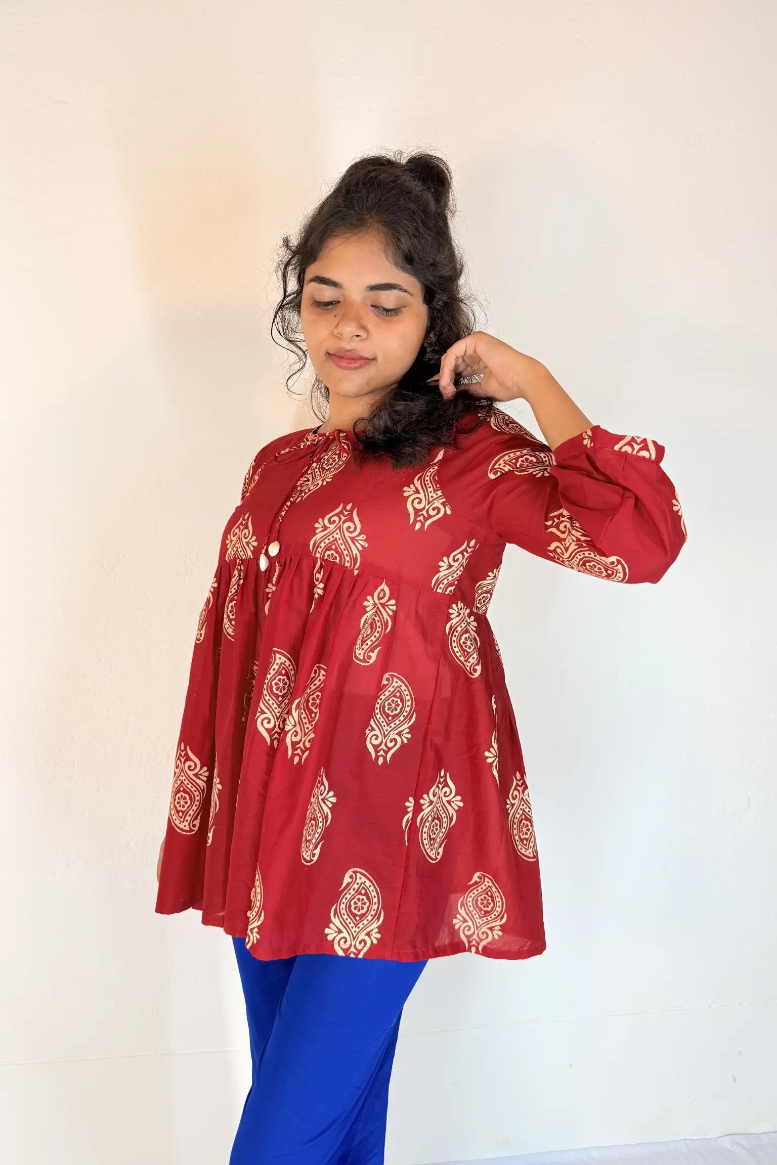 Woman wearing a red patterned top and blue pants against a white background