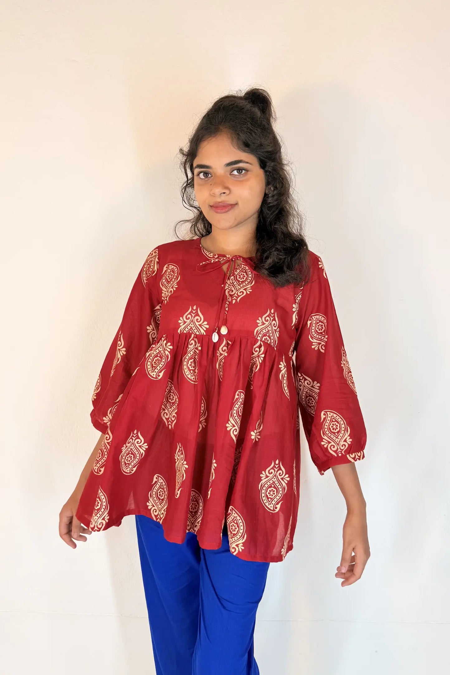 Woman wearing a red patterned top and blue pants against a white background