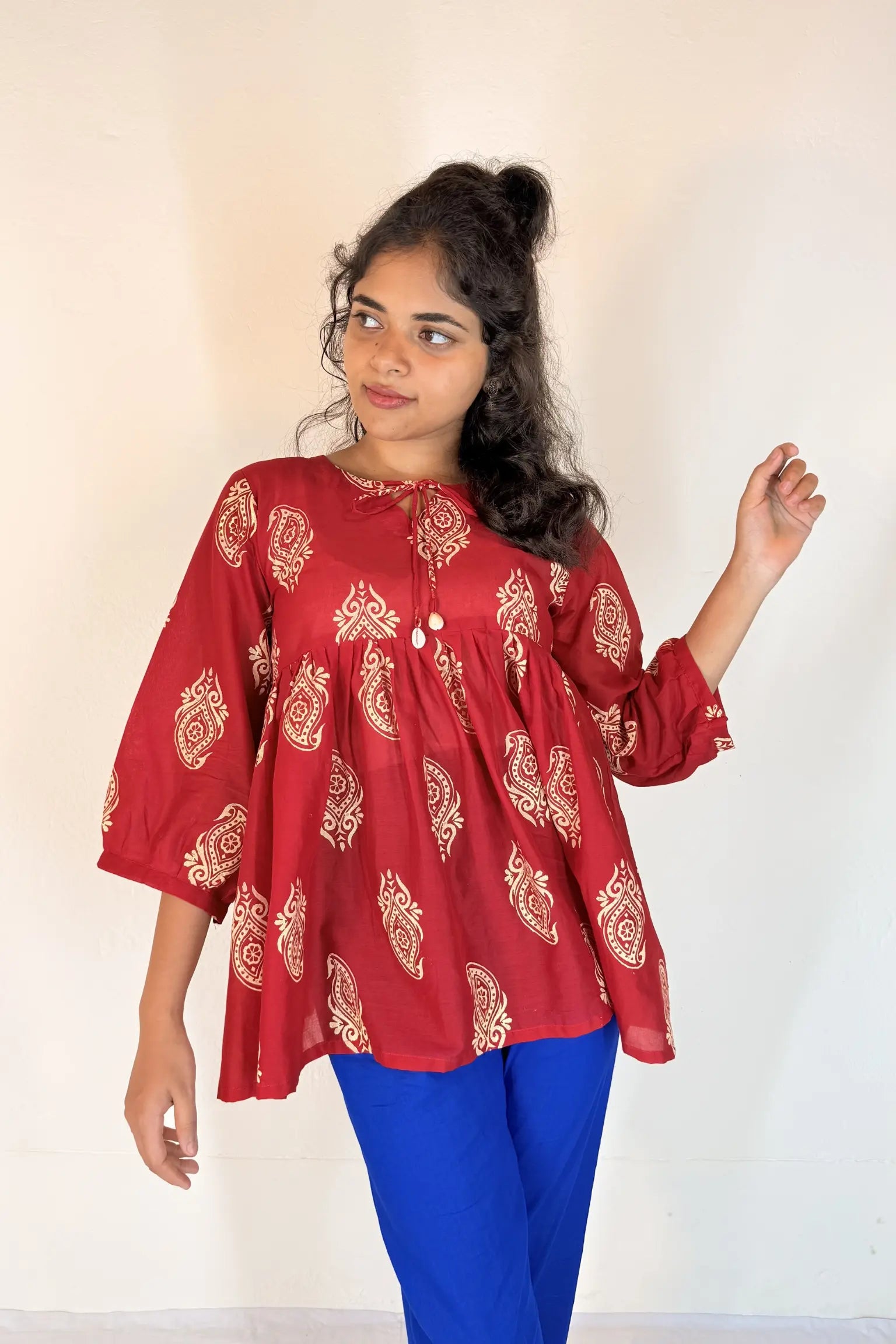 Woman wearing a red patterned top and blue pants against a white background