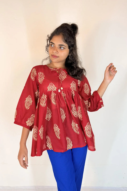 Woman wearing a red patterned top and blue pants against a white background