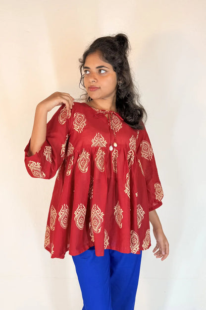 Woman wearing a red patterned top and blue pants against a white background