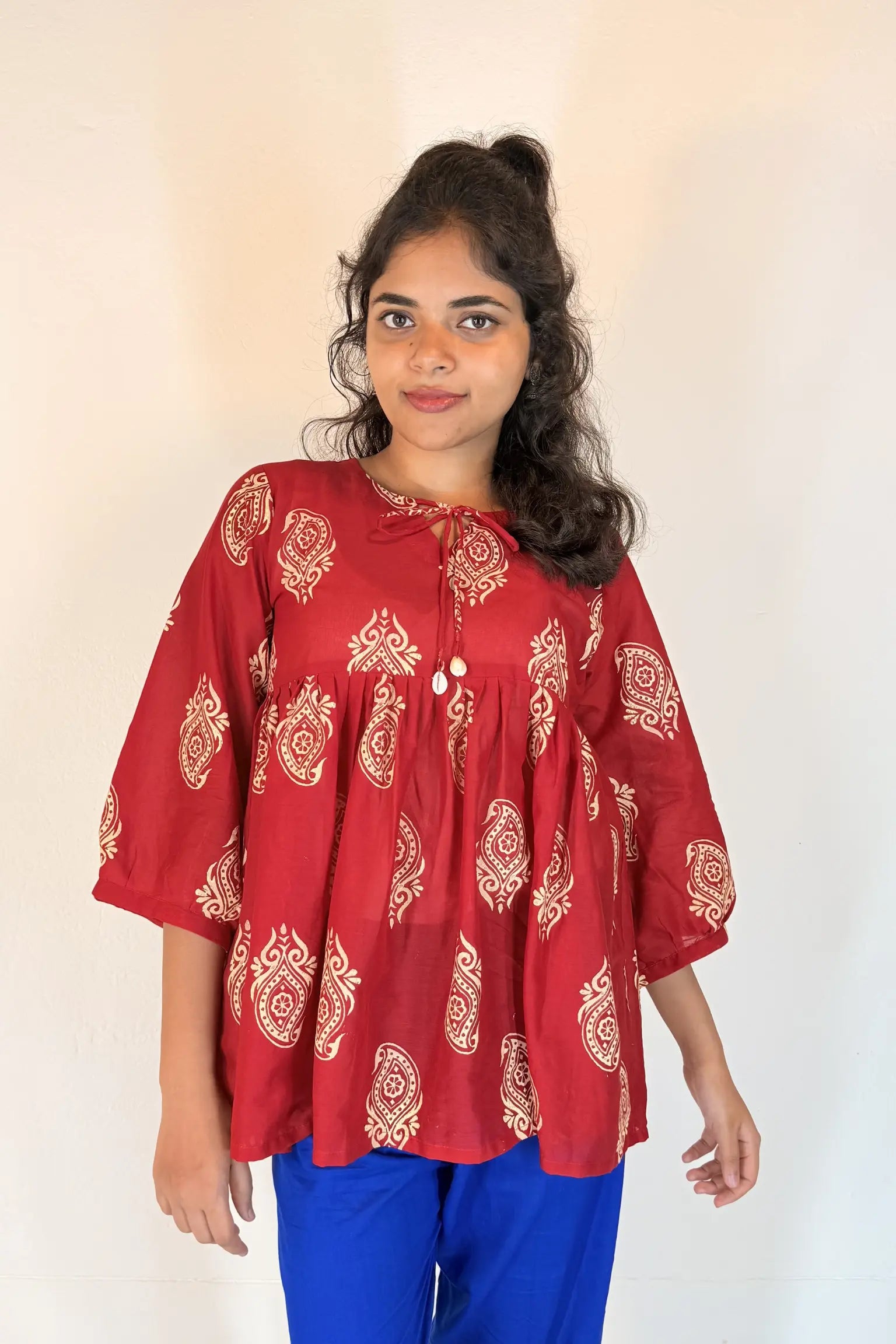 Woman wearing a red patterned blouse with blue pants against a white background