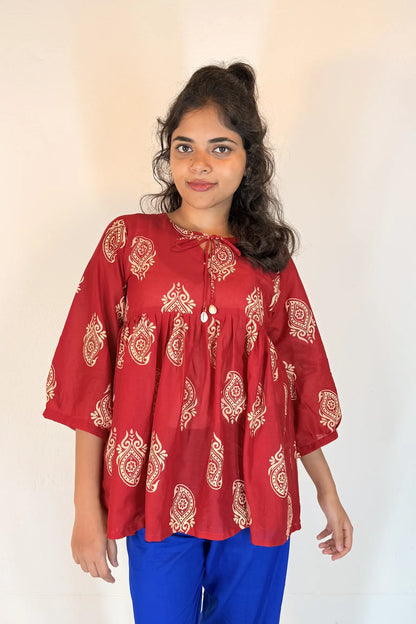 Woman wearing a red patterned blouse with blue pants against a white background
