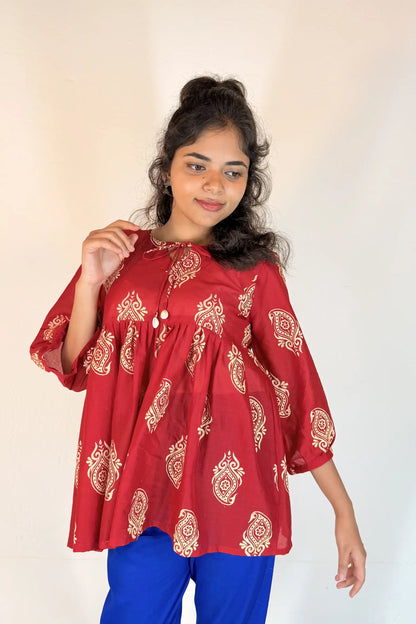 Woman wearing a red patterned top and blue pants against a plain background