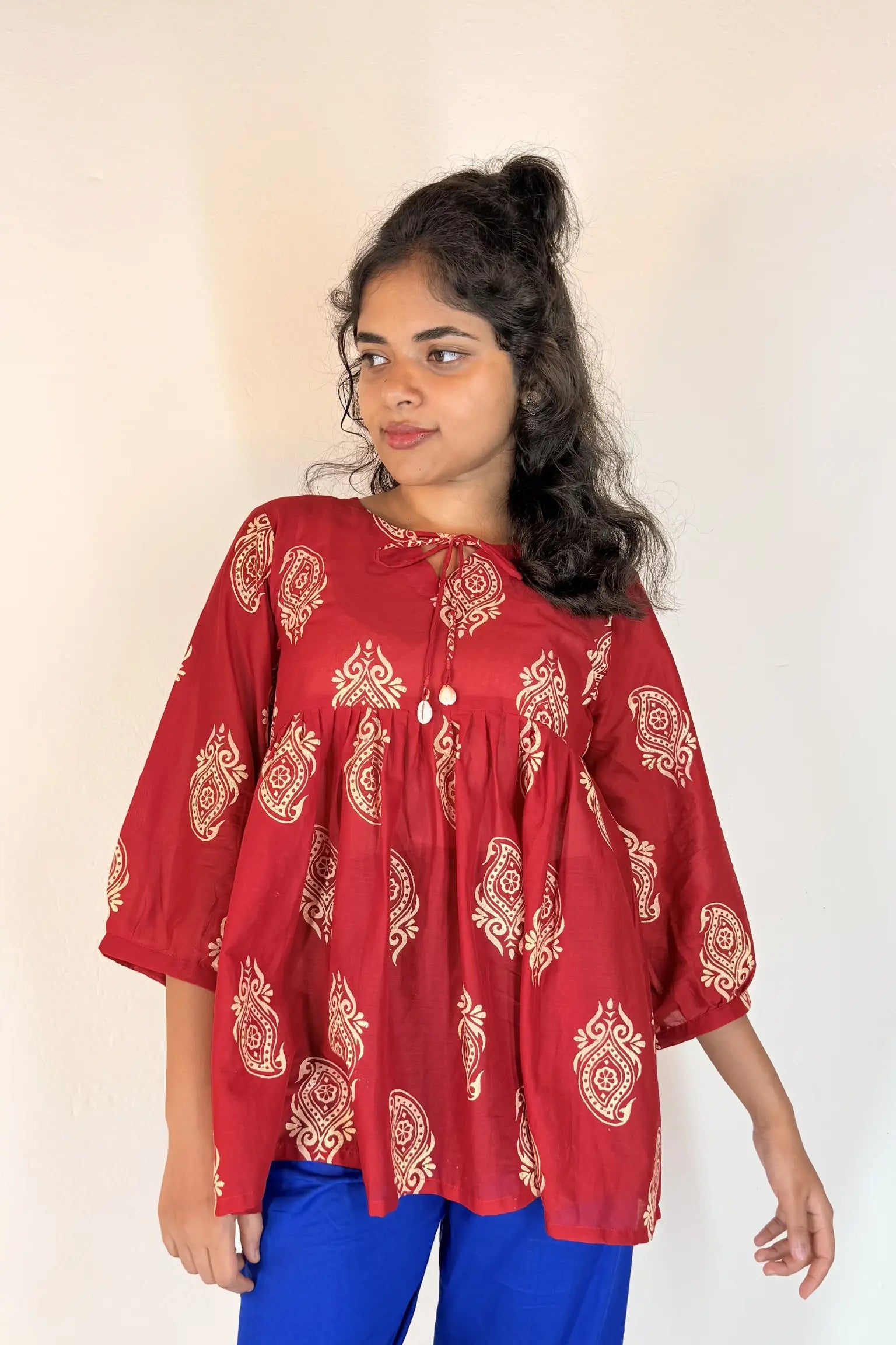 Woman wearing a red patterned top with blue pants against a white background