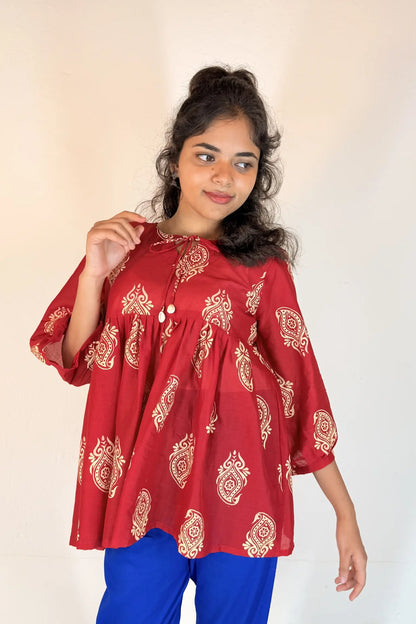 Woman wearing a red patterned top with blue pants on a plain background