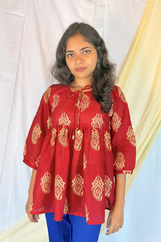 Woman wearing a red traditional top with gold patterns against a white background