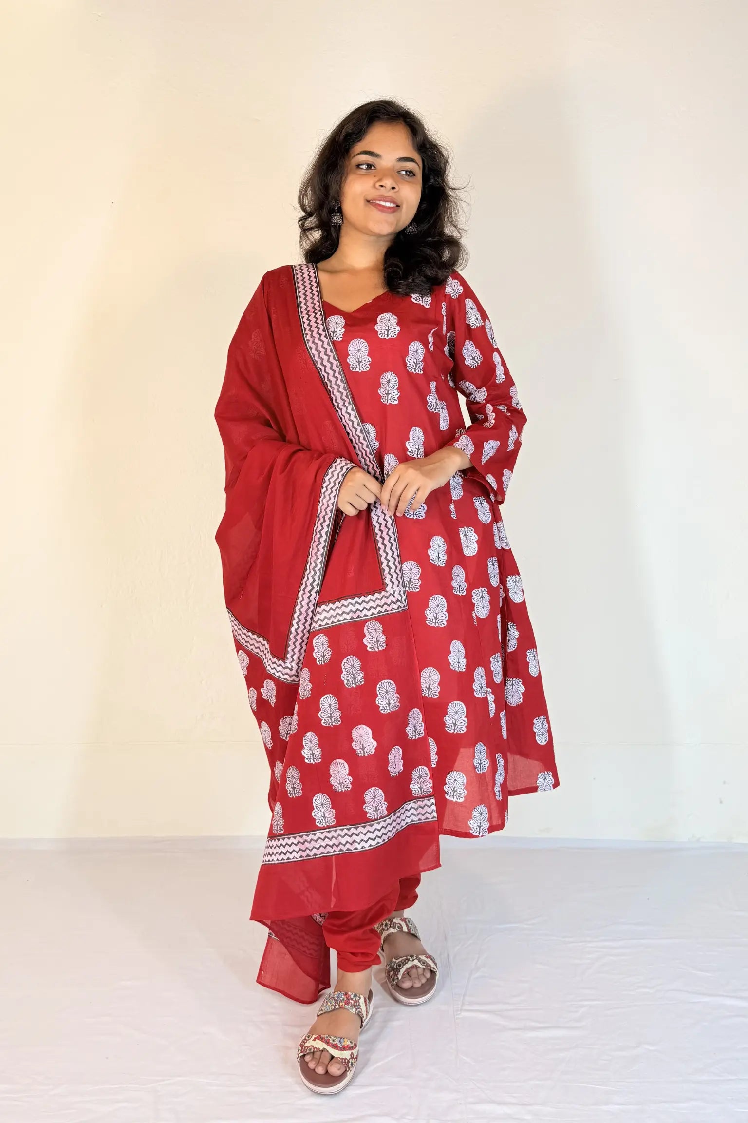 Woman wearing a red traditional outfit with white patterns on a plain background