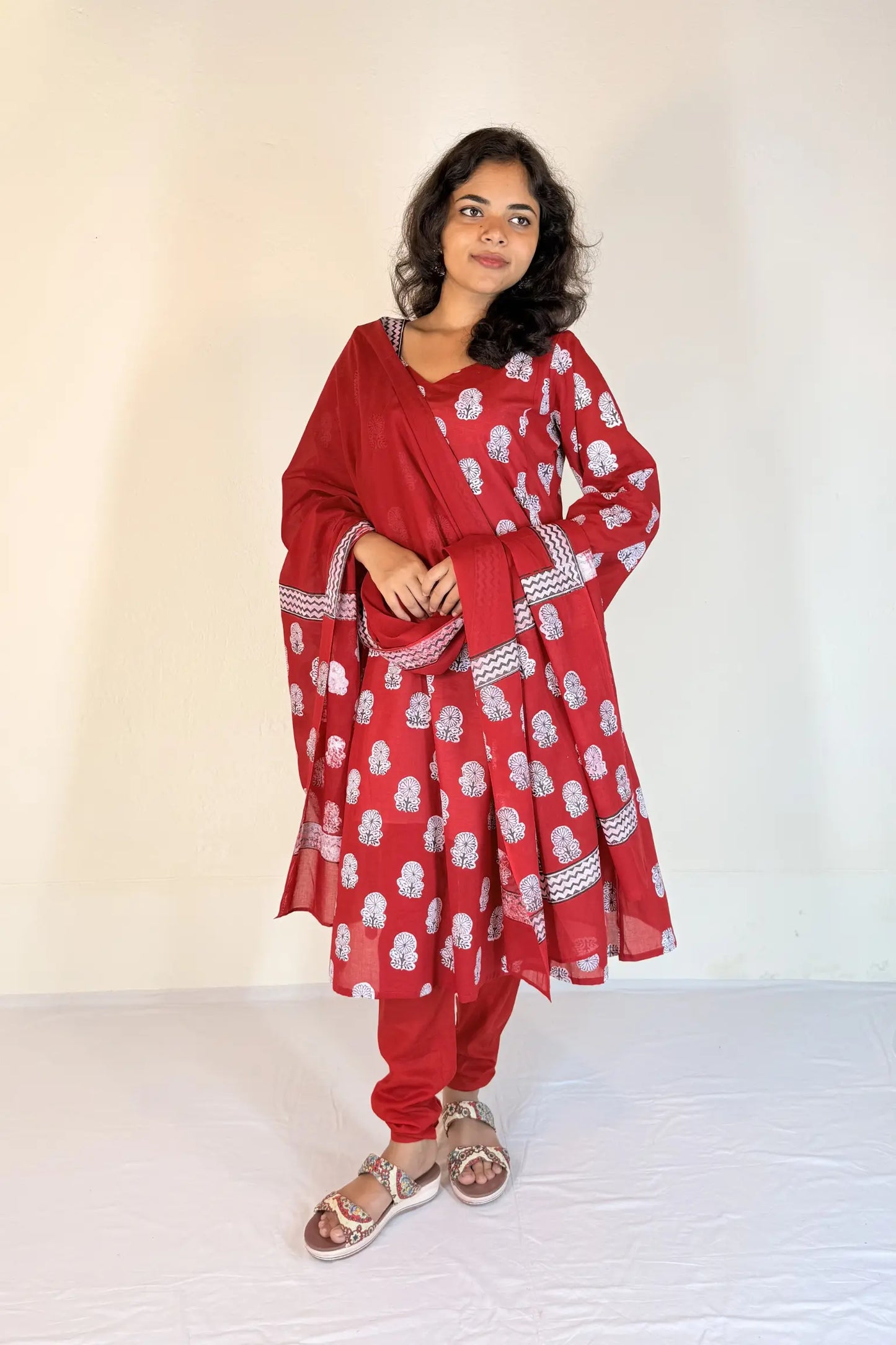 Woman wearing a red traditional outfit with white patterns on a plain background