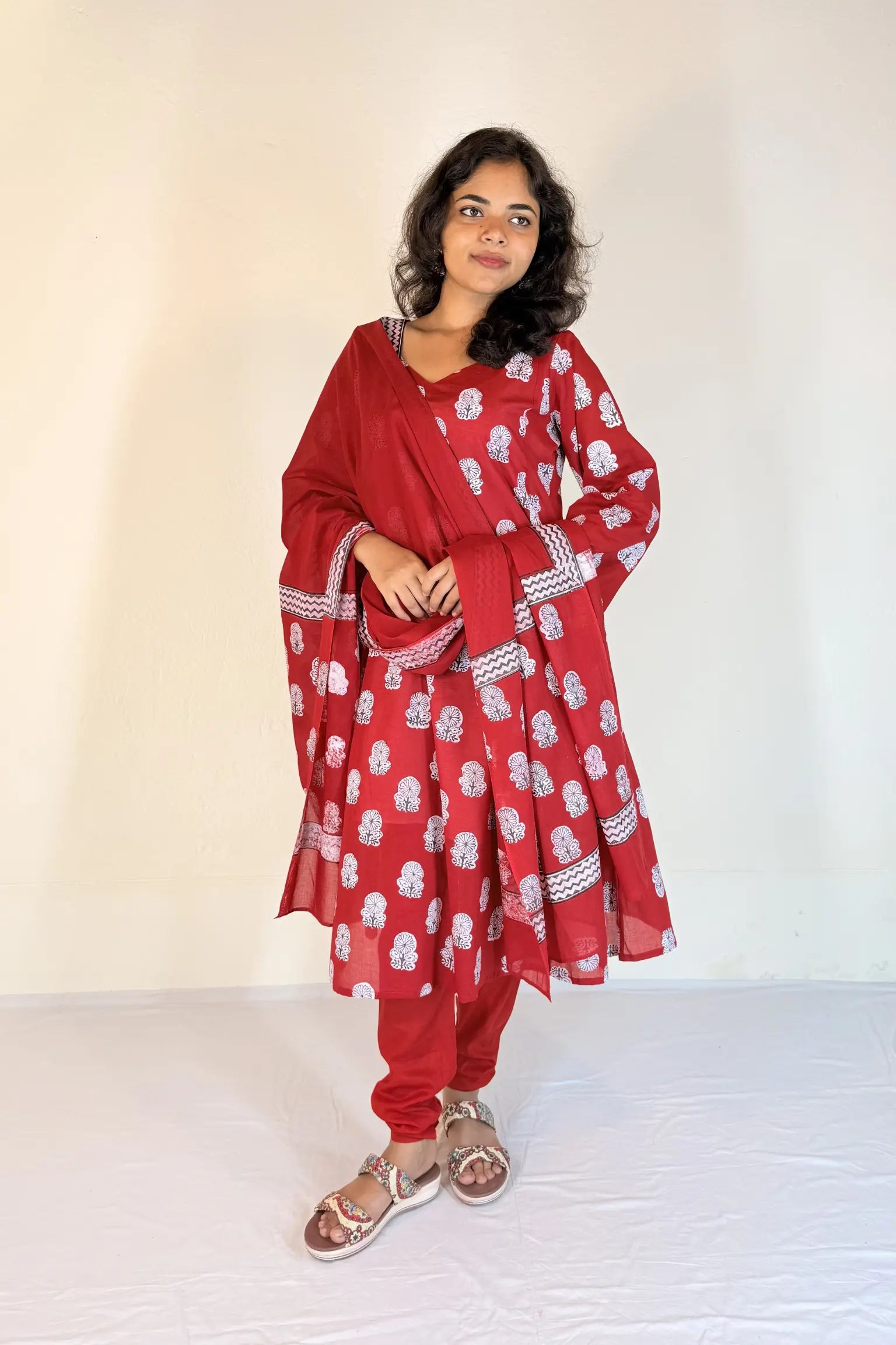 Woman wearing a red traditional outfit with white patterns on a plain background