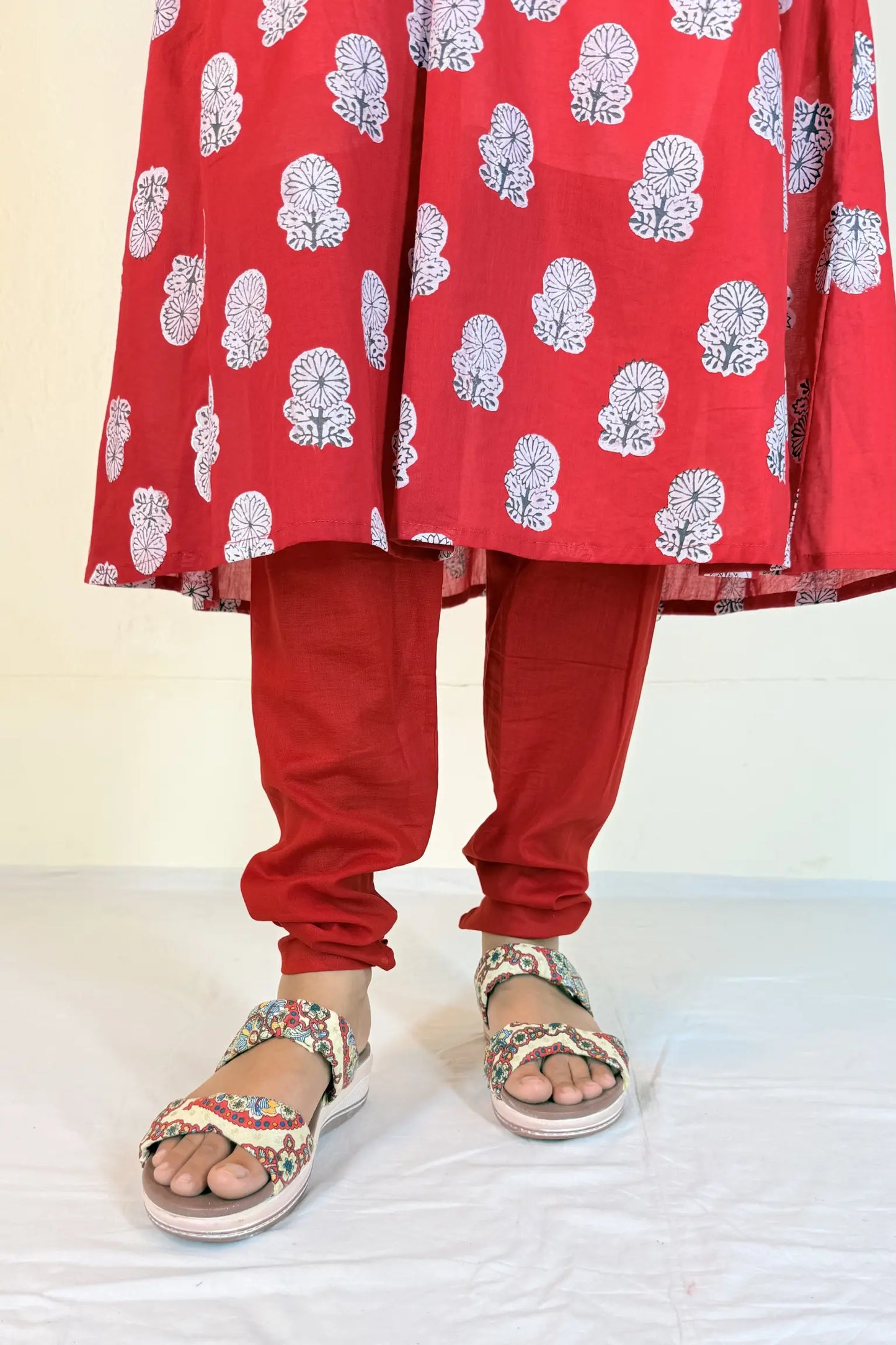 Red traditional outfit with white patterns and sandals on a light background