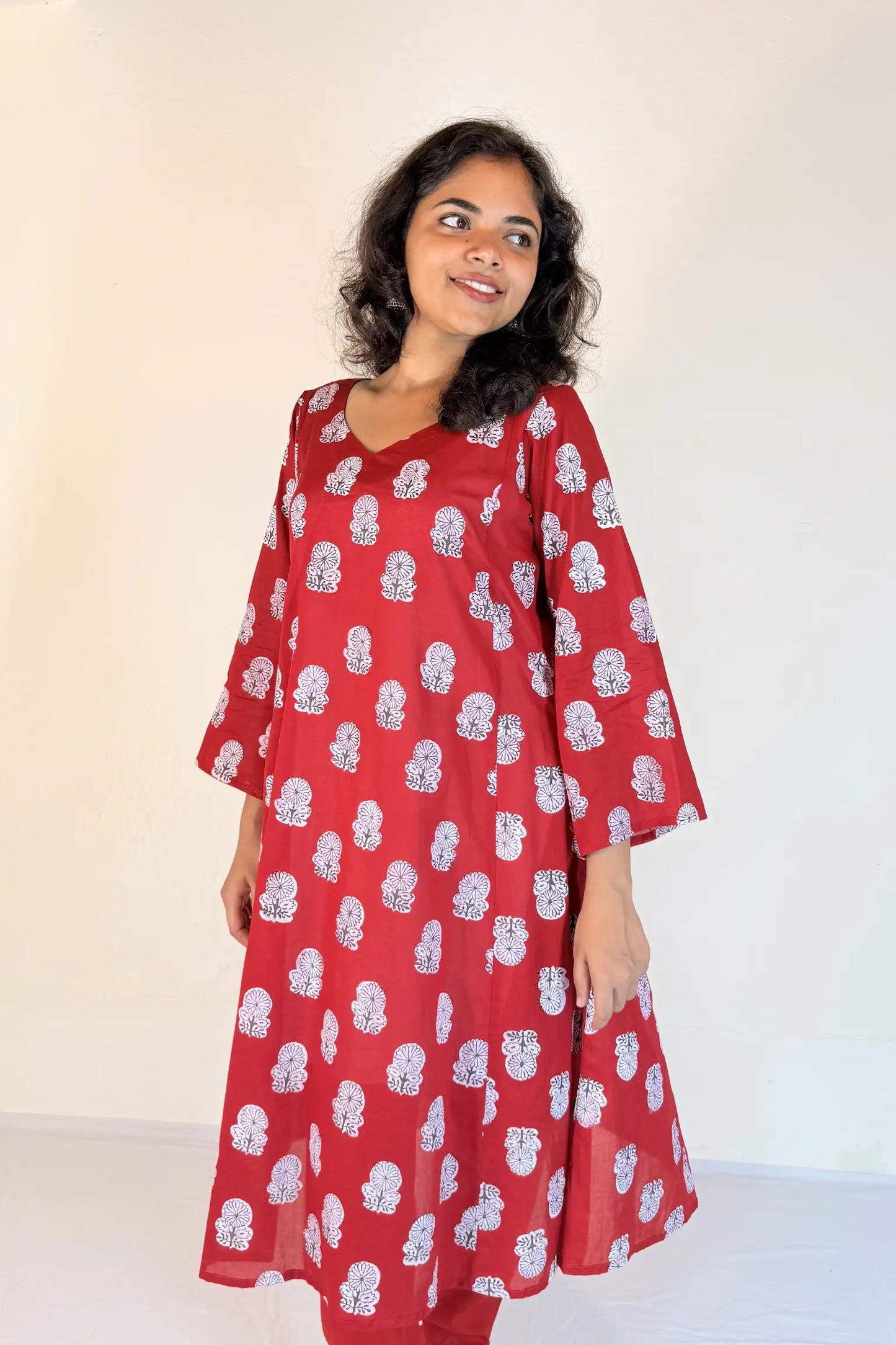 Woman wearing a red dress with white patterns against a plain background