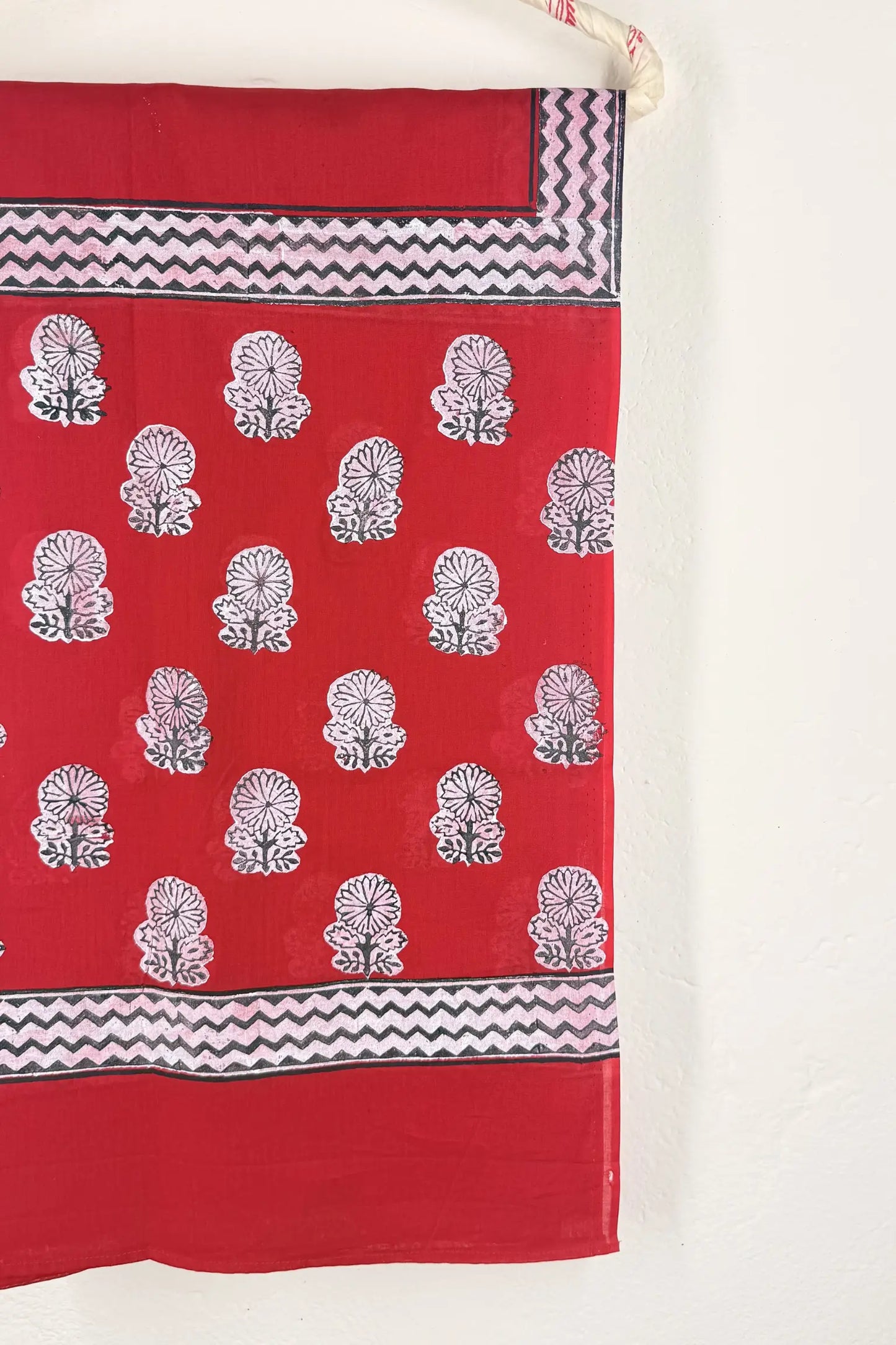 Red fabric with white floral patterns and black zigzag borders on a white background