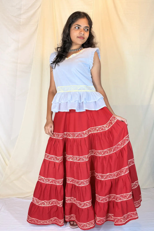 Woman wearing a white top and red skirt with white patterns against a plain background