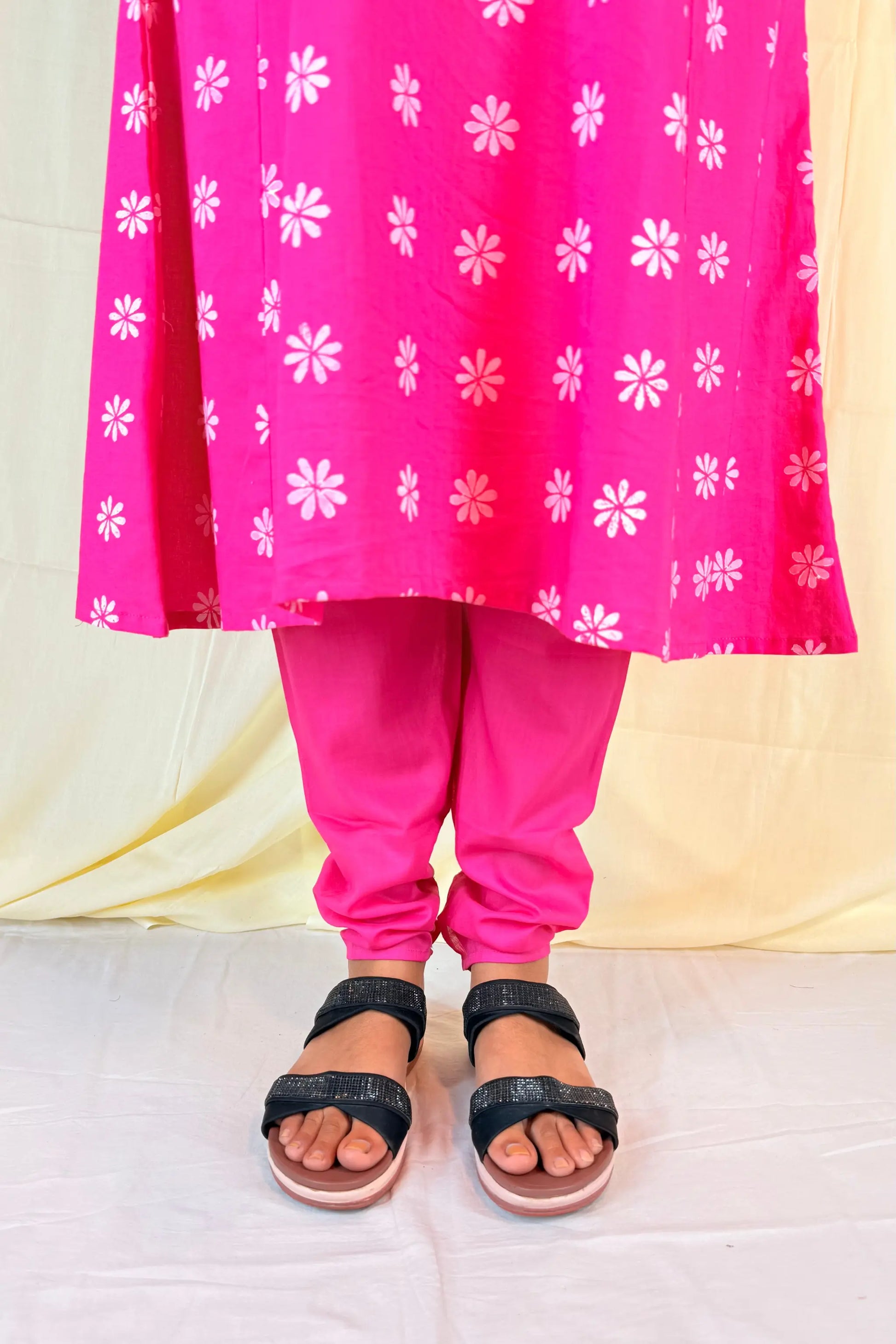 Person wearing a bright pink traditional outfit with white floral patterns on a light yellow background.