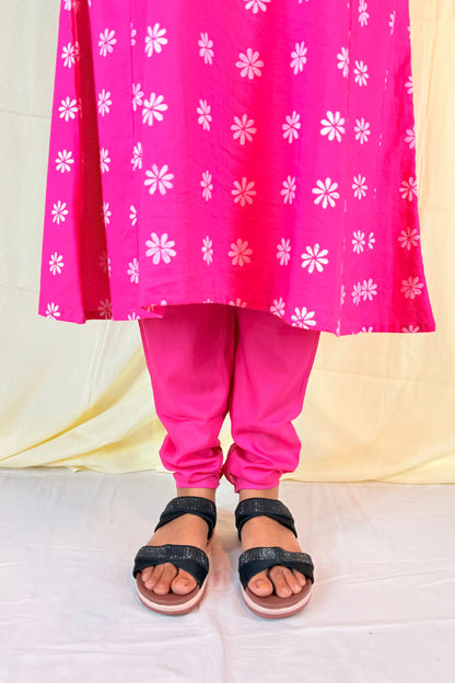 Person wearing a bright pink traditional outfit with white floral patterns on a light yellow background.