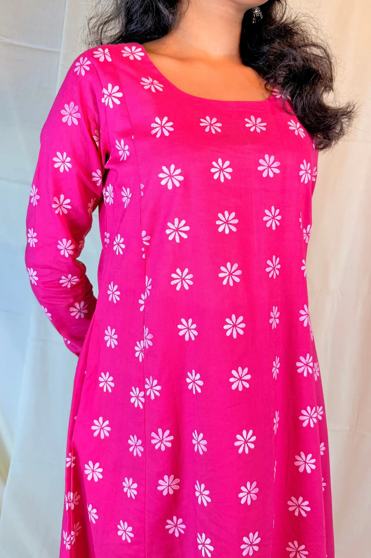Pink dress with white floral patterns worn by a person against a neutral background