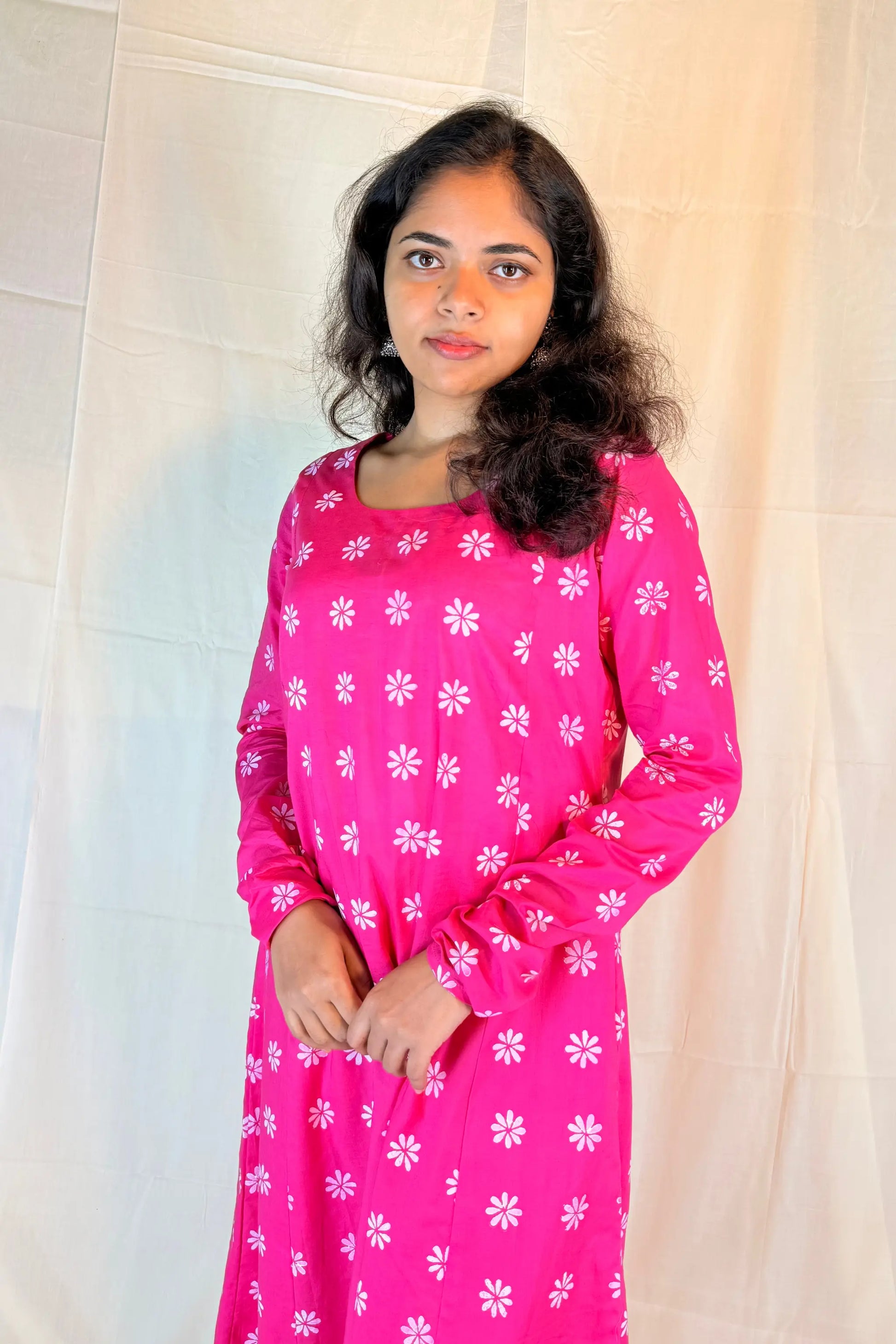 Woman wearing a pink dress with white floral patterns against a plain background
