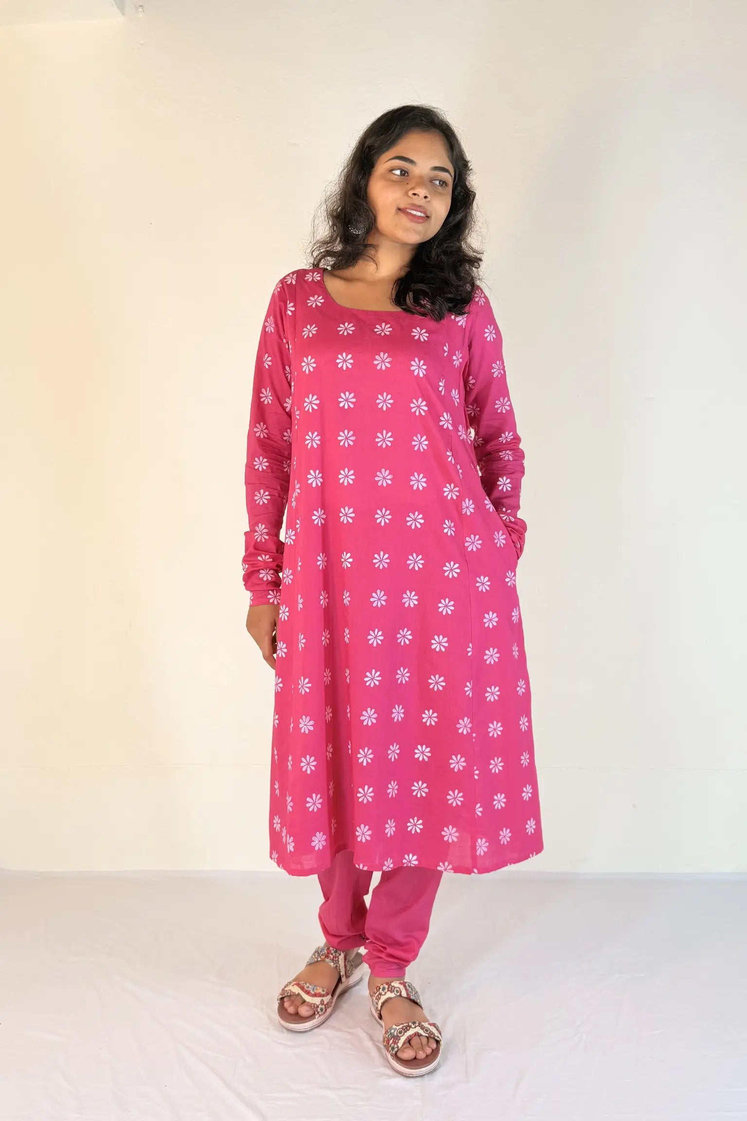 Woman wearing a pink kurta with white floral patterns on a plain background