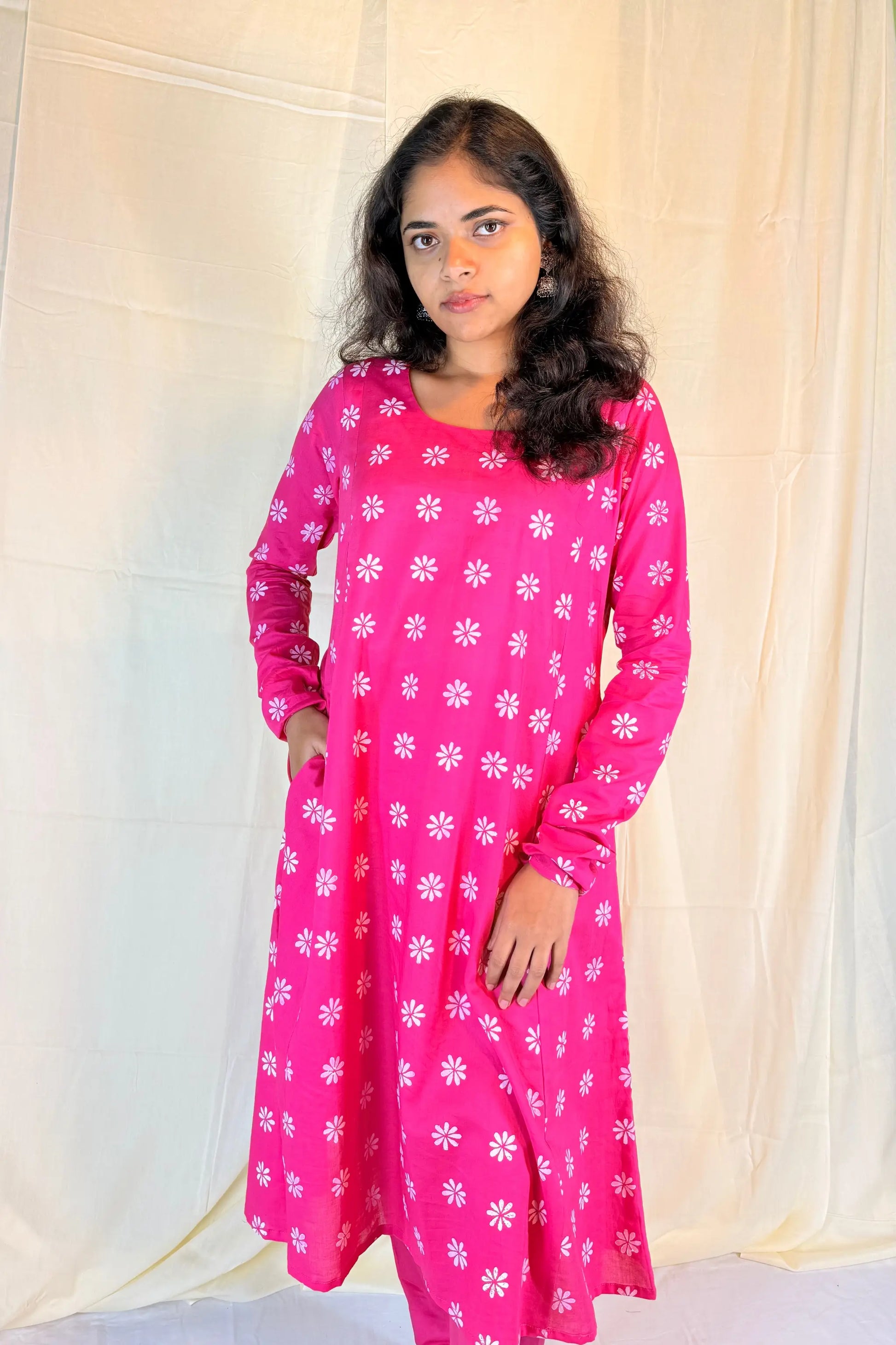 Woman wearing a pink dress with white floral patterns against a plain background