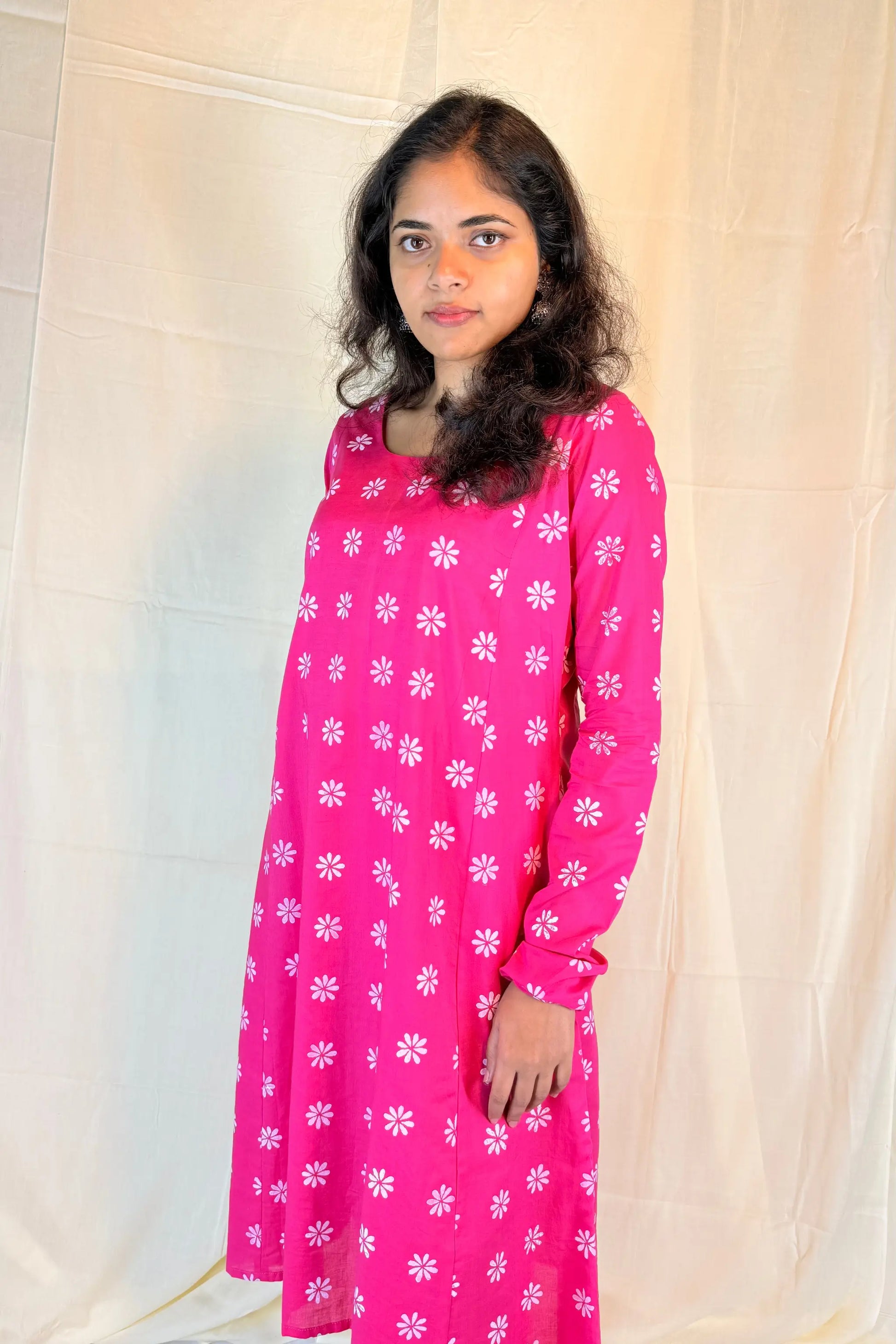 Woman wearing a pink dress with white floral pattern against a plain background