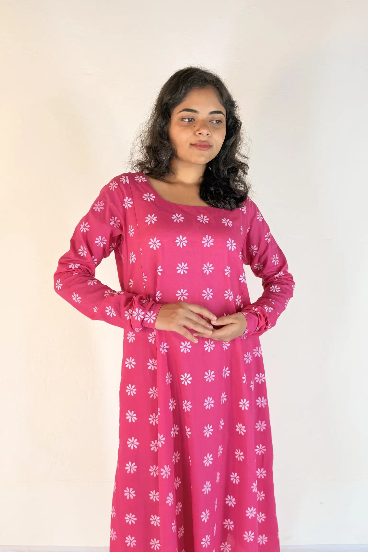 Woman wearing a pink dress with white floral patterns against a plain background