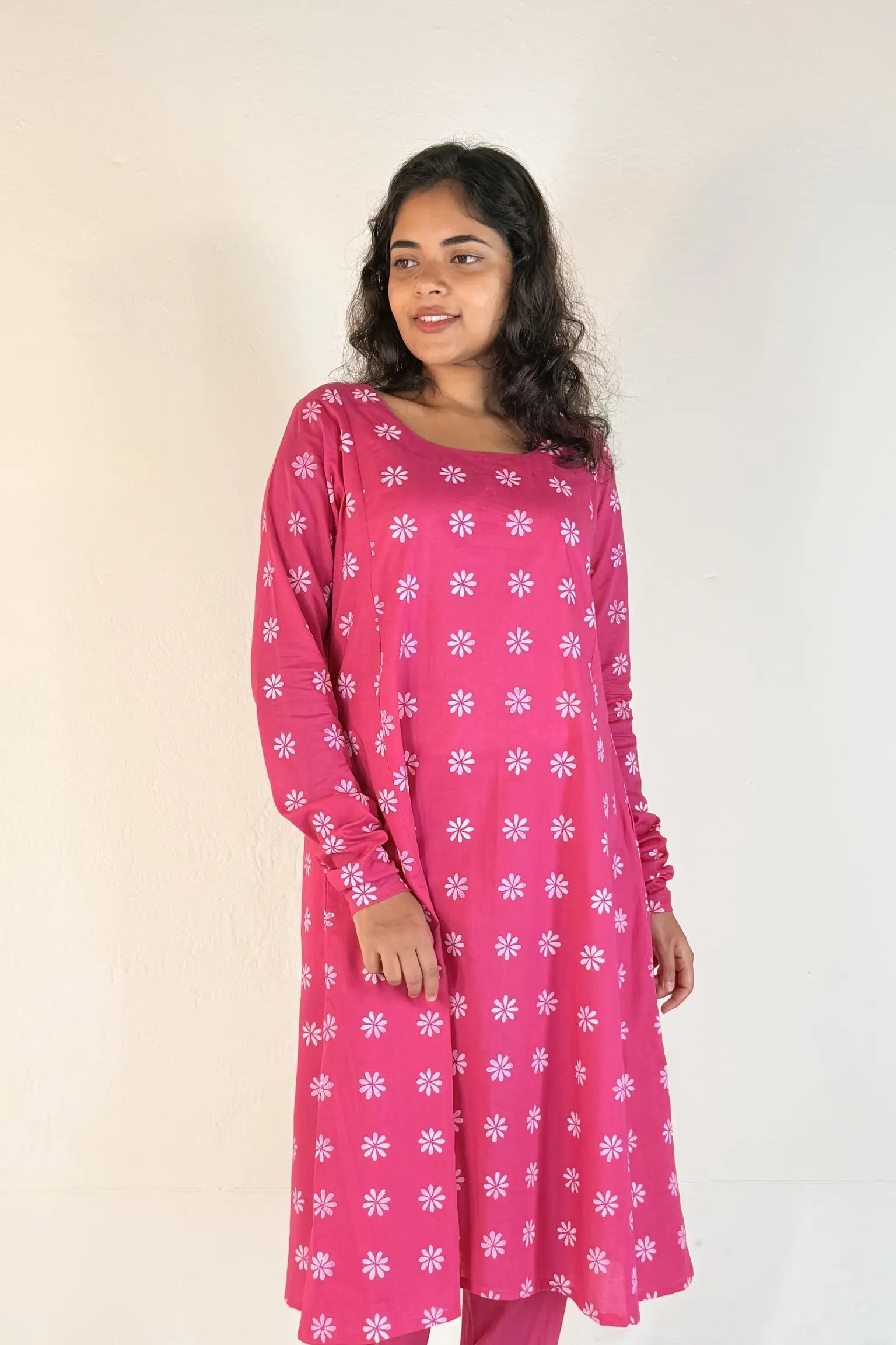 Woman wearing a pink kurta with white floral patterns on a plain background