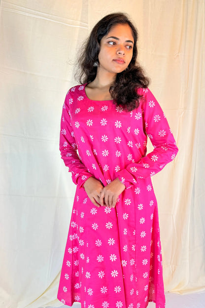 Woman wearing a pink dress with white floral patterns against a plain background
