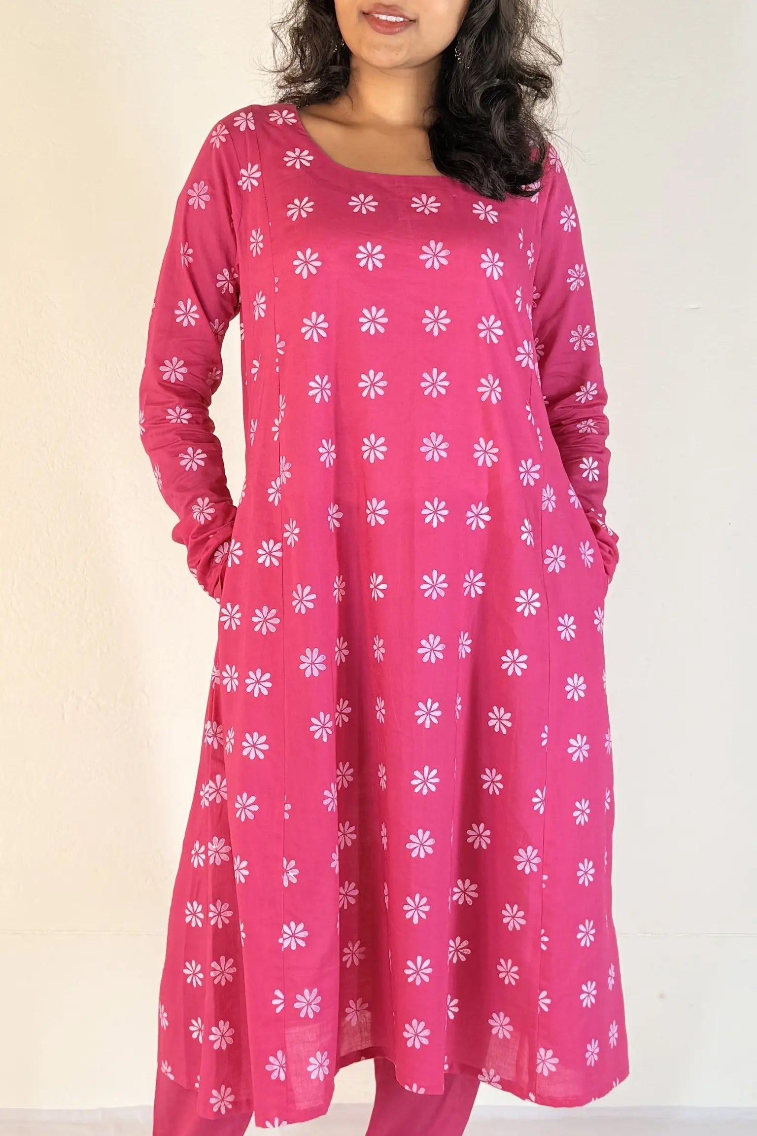 Woman wearing a pink dress with white floral pattern on a plain background