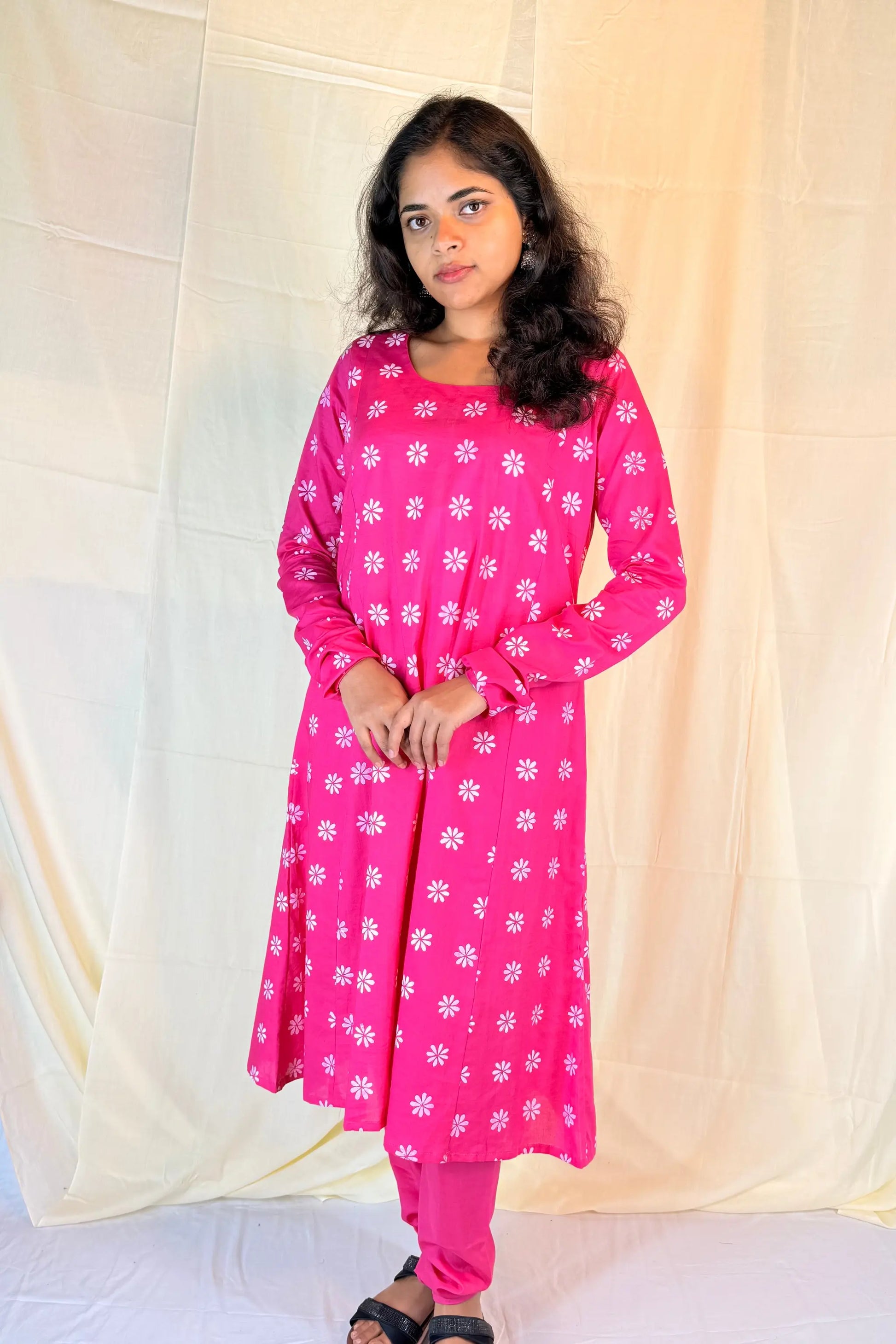 Woman wearing a pink floral dress against a white curtain background
