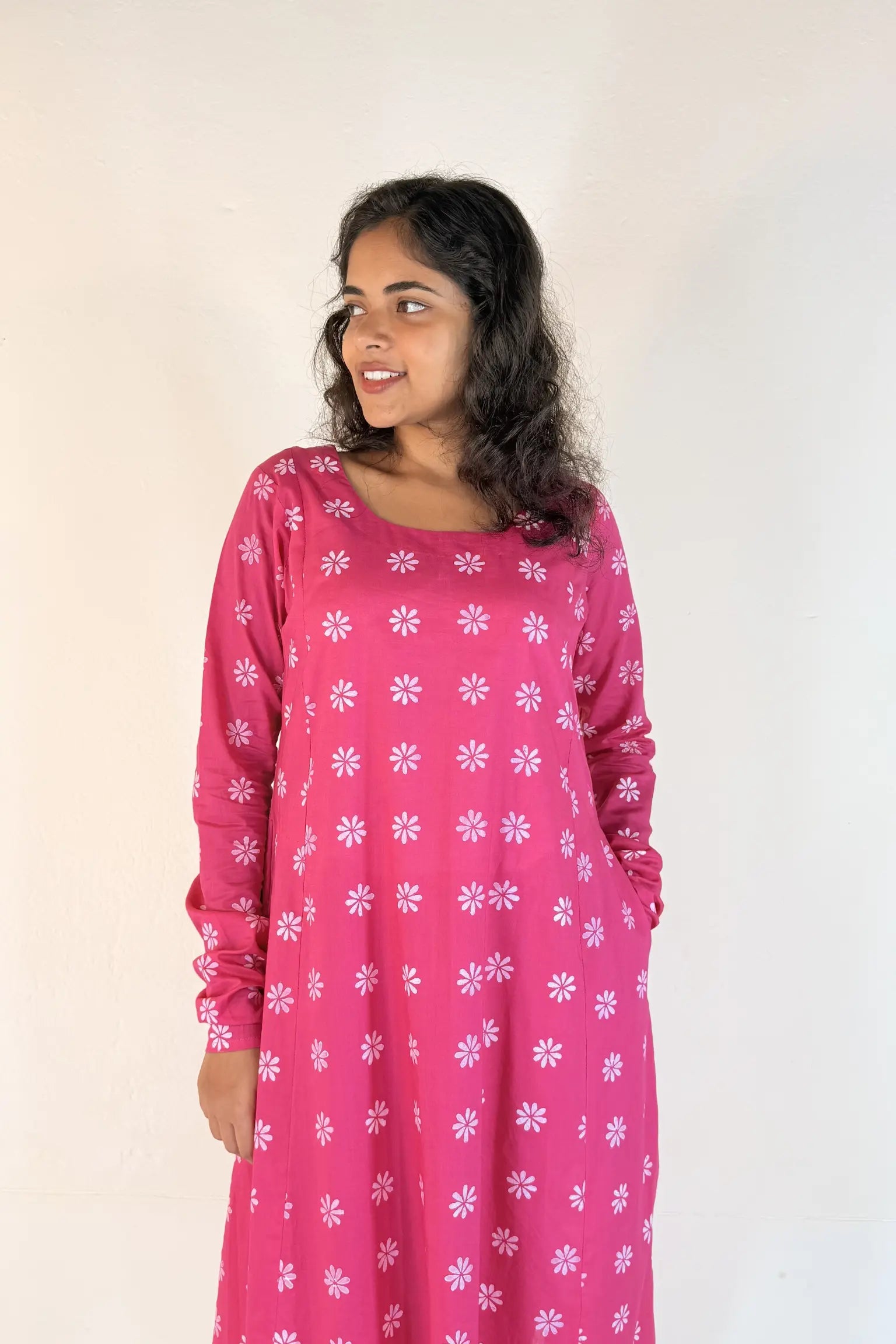 Woman wearing a pink dress with white floral patterns against a plain background