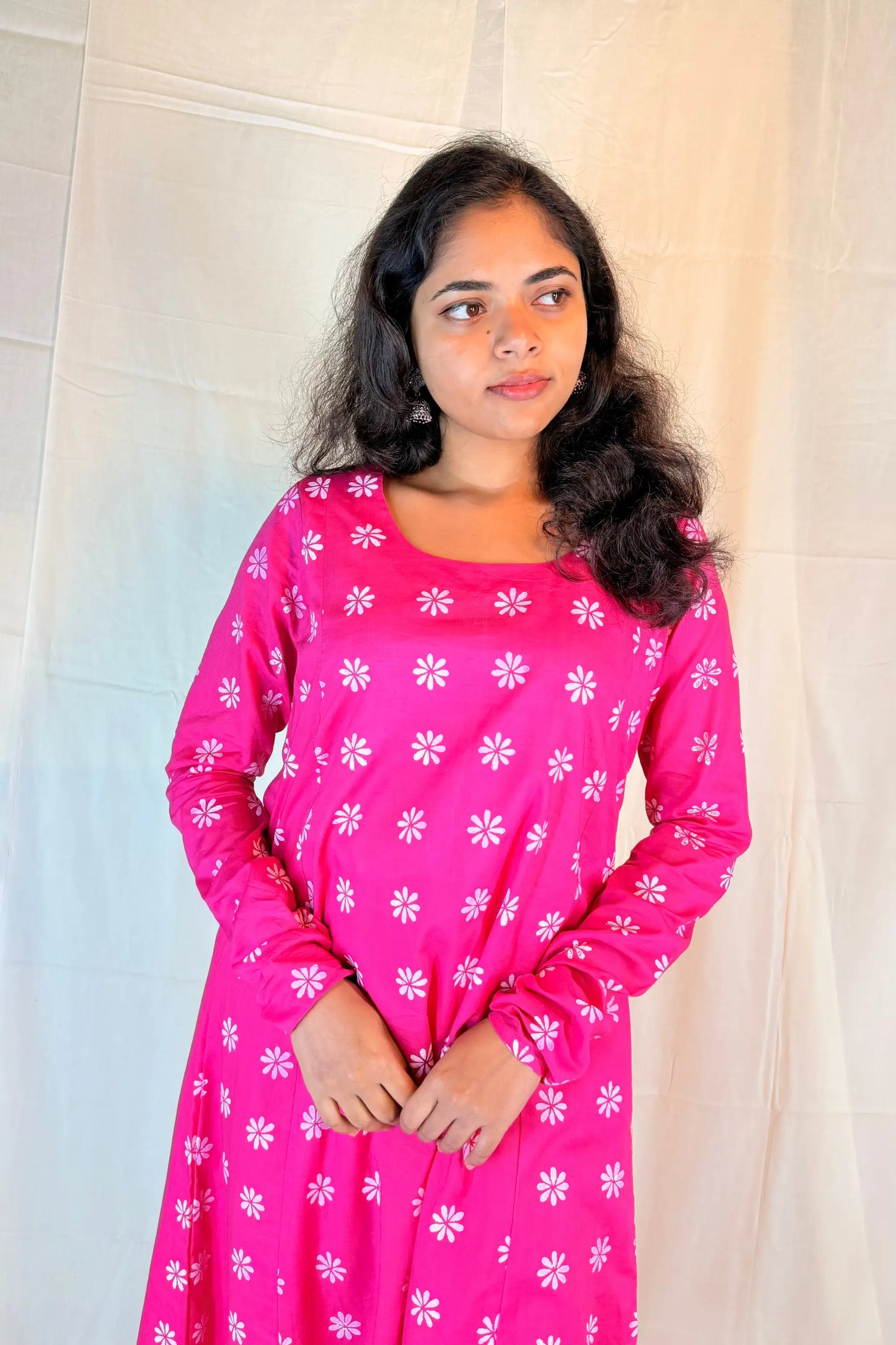 Woman wearing a pink dress with white floral patterns against a neutral background