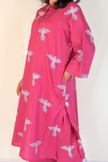 Person wearing a pink outfit with white floral patterns on a plain background