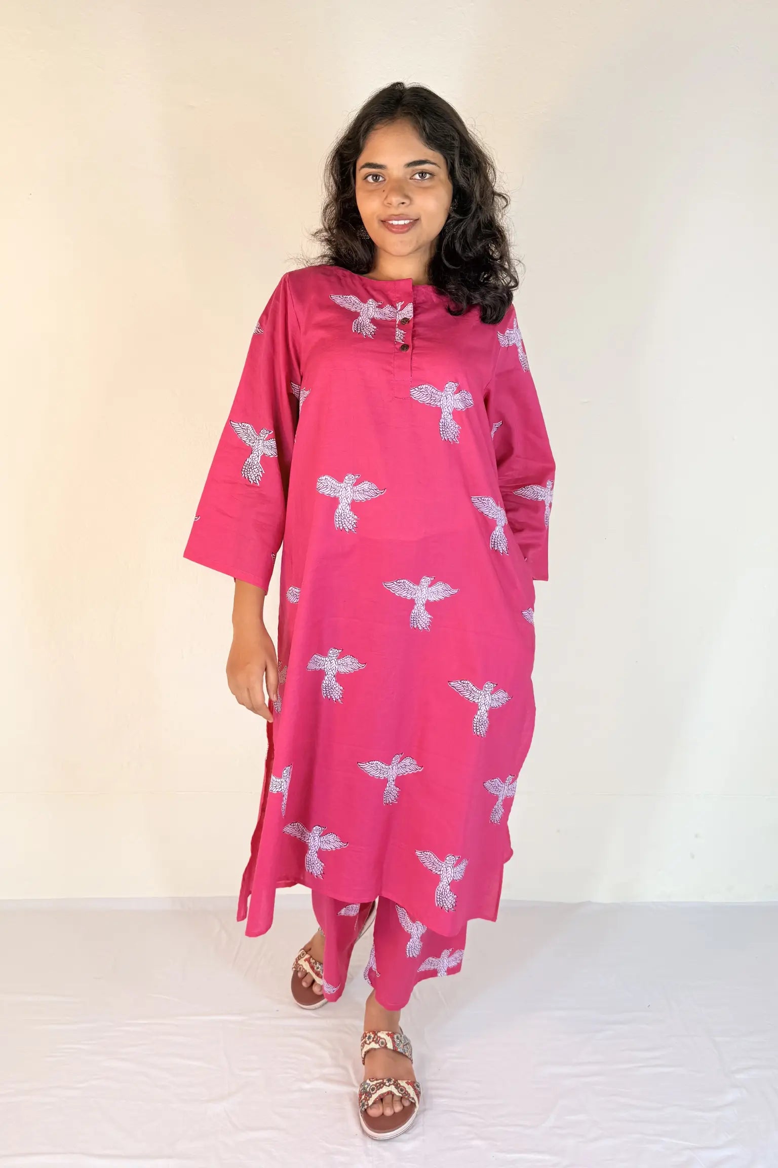 Woman wearing a pink dress with white patterns against a plain background