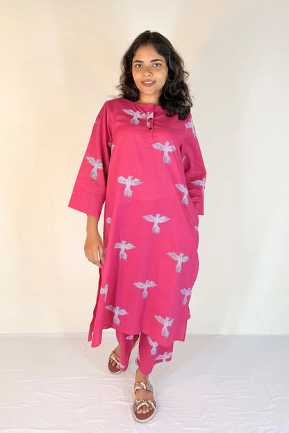 Woman wearing a pink dress with white patterns against a plain background