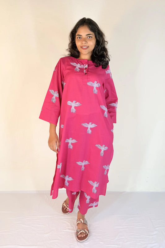 Woman wearing a pink dress with white patterns against a plain background