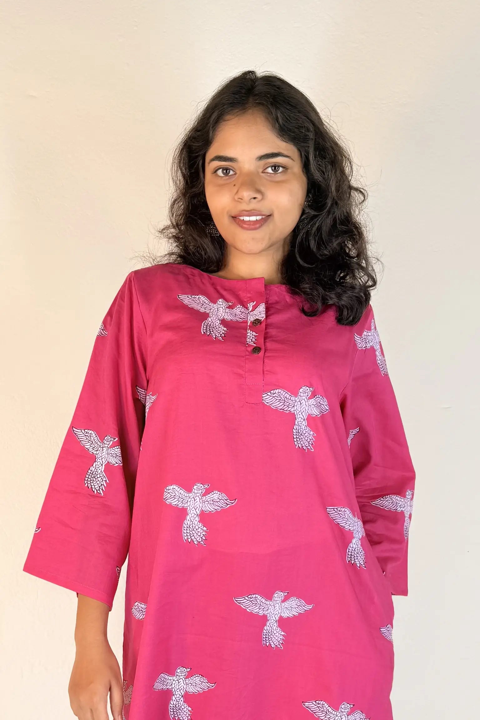 Woman wearing a pink kurta with white floral patterns on a beige background