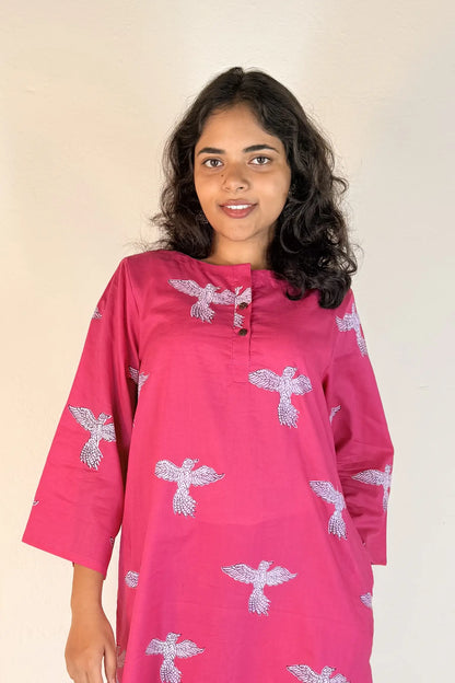 Woman wearing a pink kurta with white floral patterns on a beige background