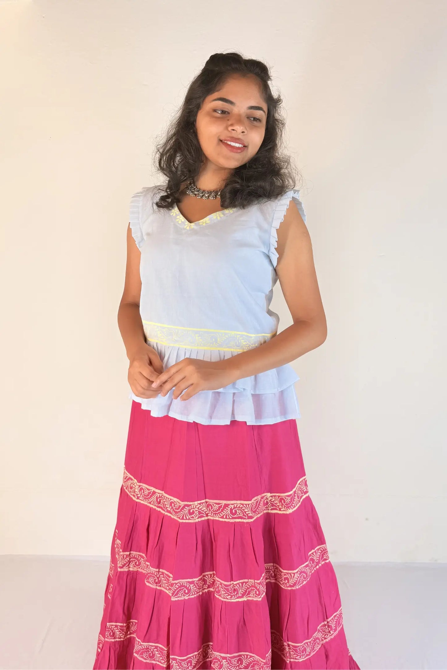 Woman wearing a white top and pink skirt with white patterns on a white background