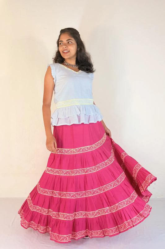 Woman wearing a white top and pink skirt with white patterns on a white background