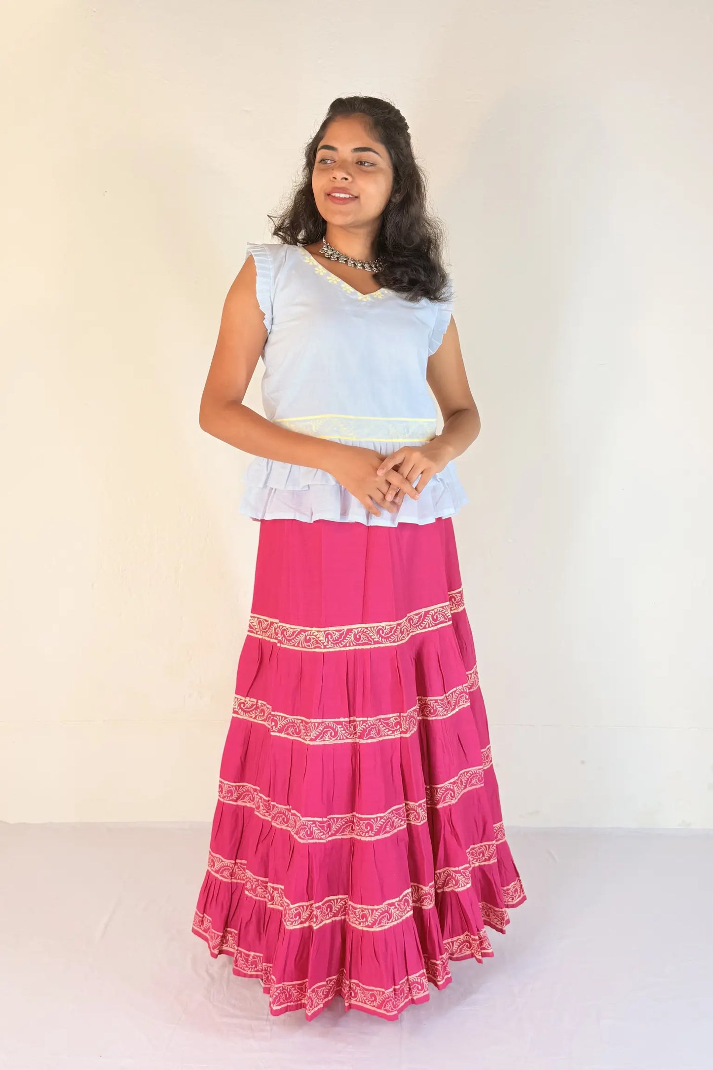 Woman wearing a white top and pink skirt with white patterns on a white background
