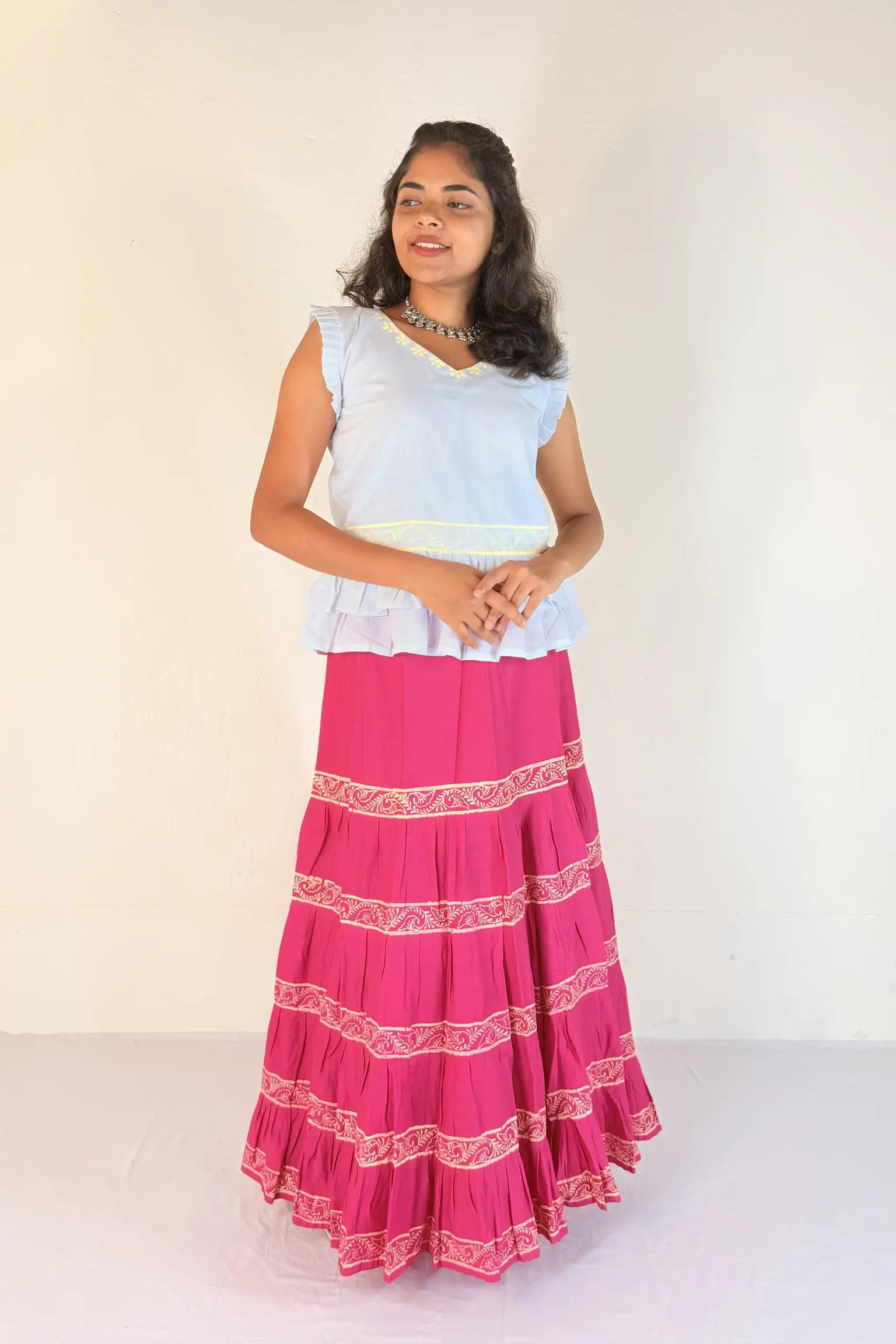Woman wearing a white top and pink skirt with white patterns on a white background