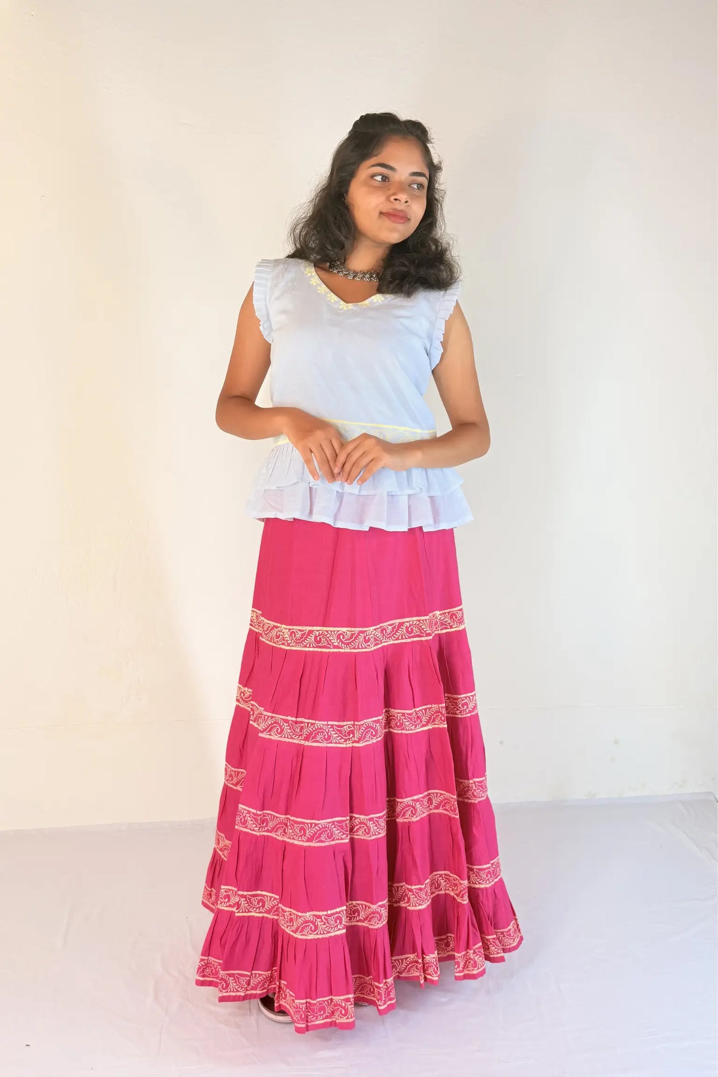 Woman wearing a white top and pink skirt with white patterns on a white background