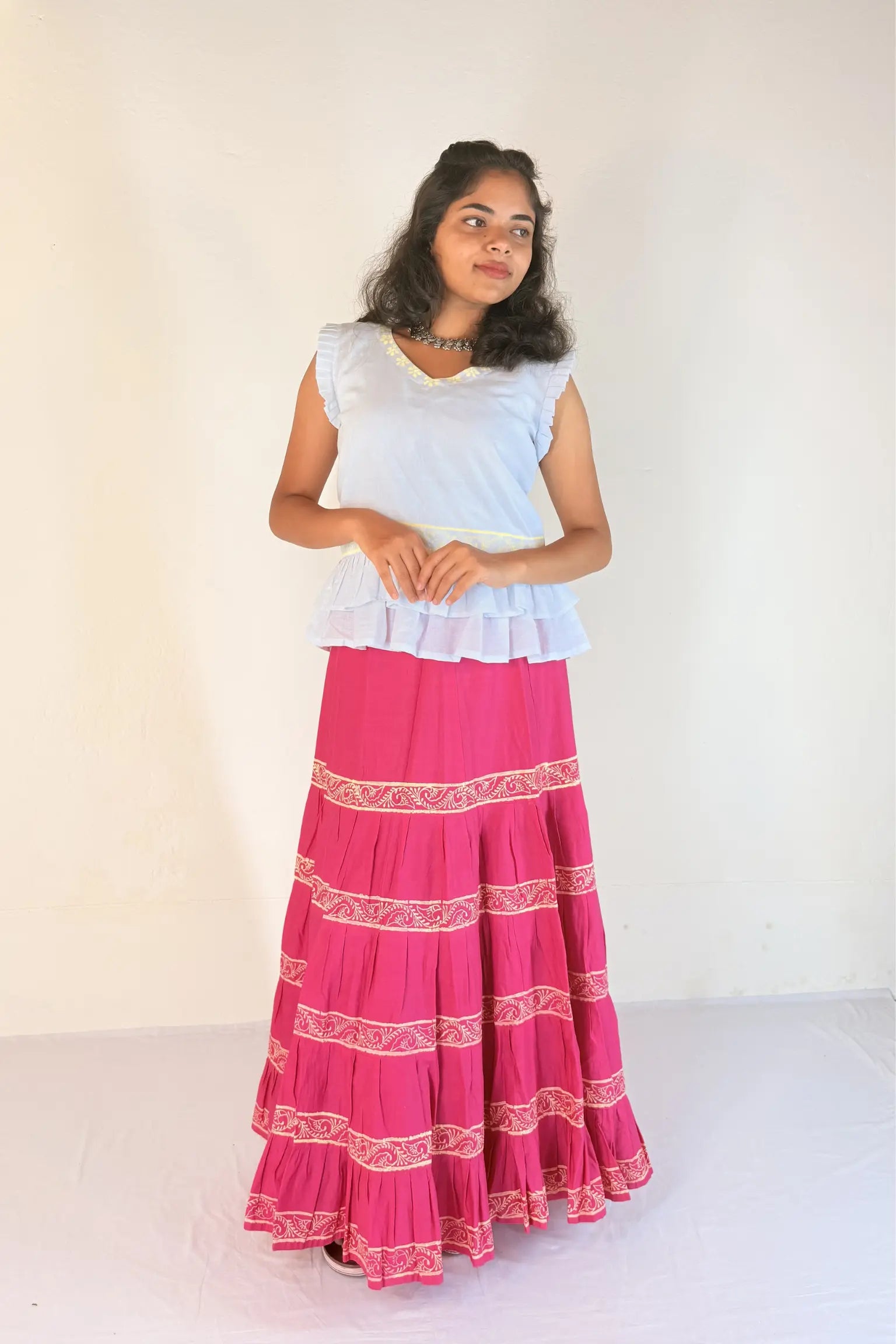 Woman wearing a white top and pink skirt with white patterns on a white background