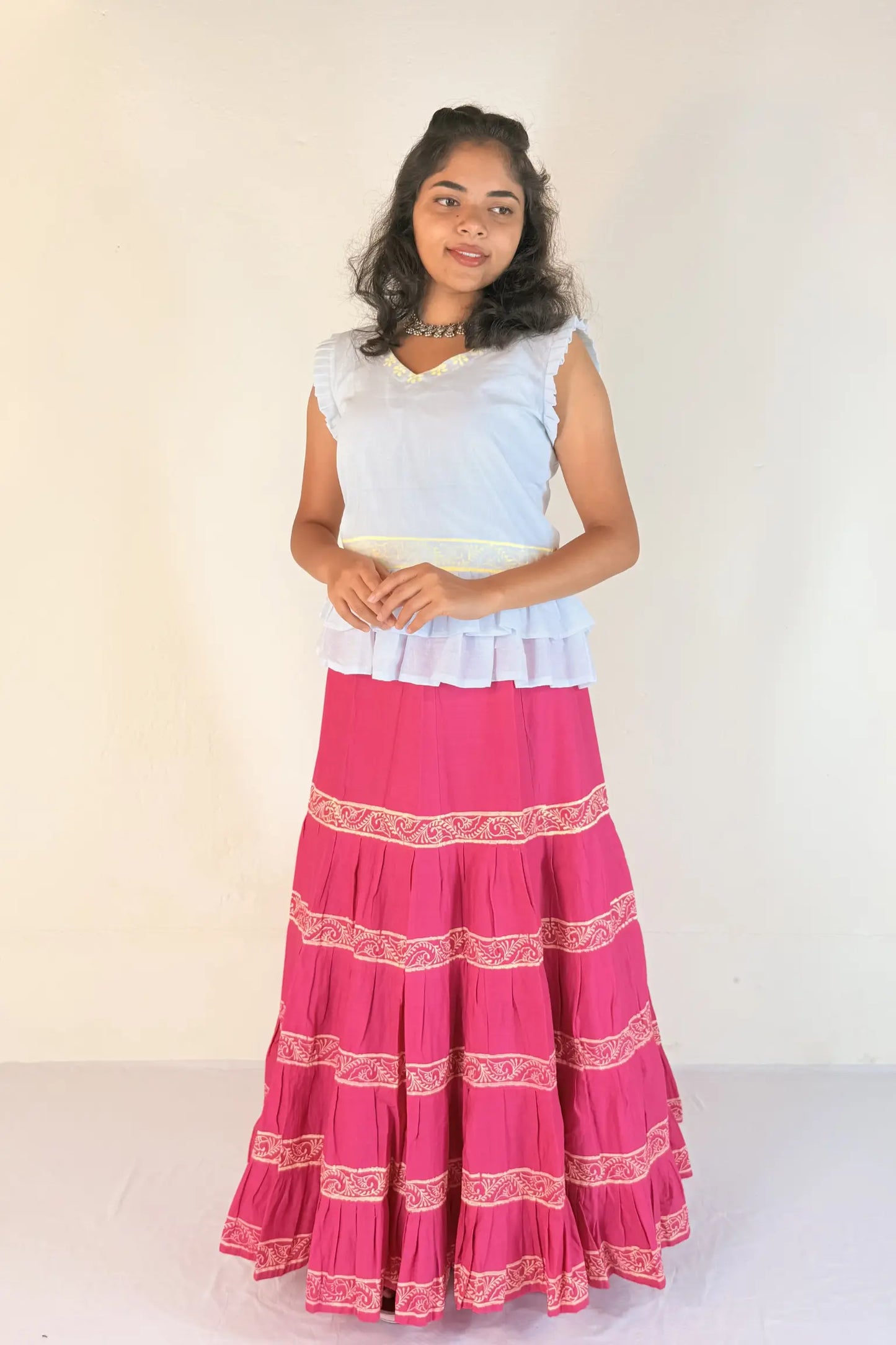 Woman wearing a white top and pink skirt with white patterns on a white background