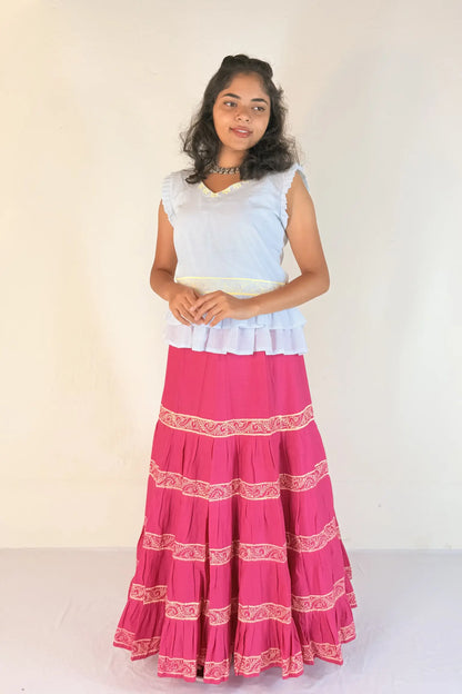 Woman wearing a white top and pink skirt with white patterns on a white background