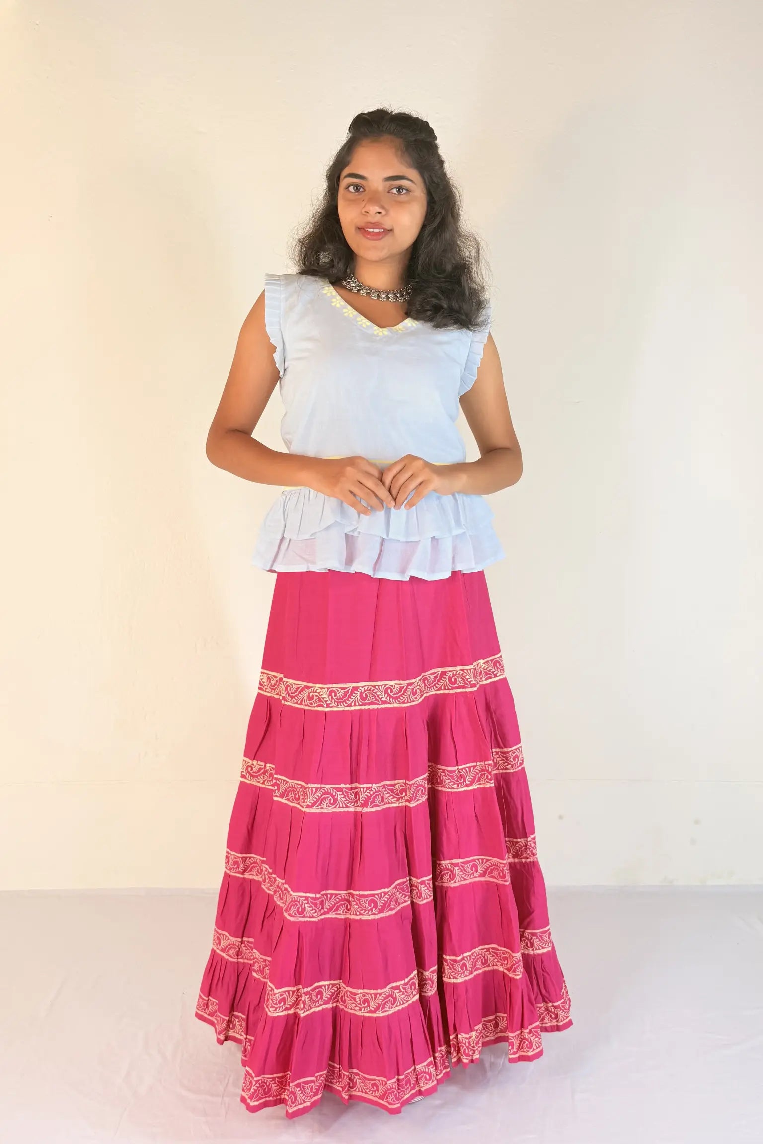 Woman wearing a white top and pink skirt with white patterns on a white background